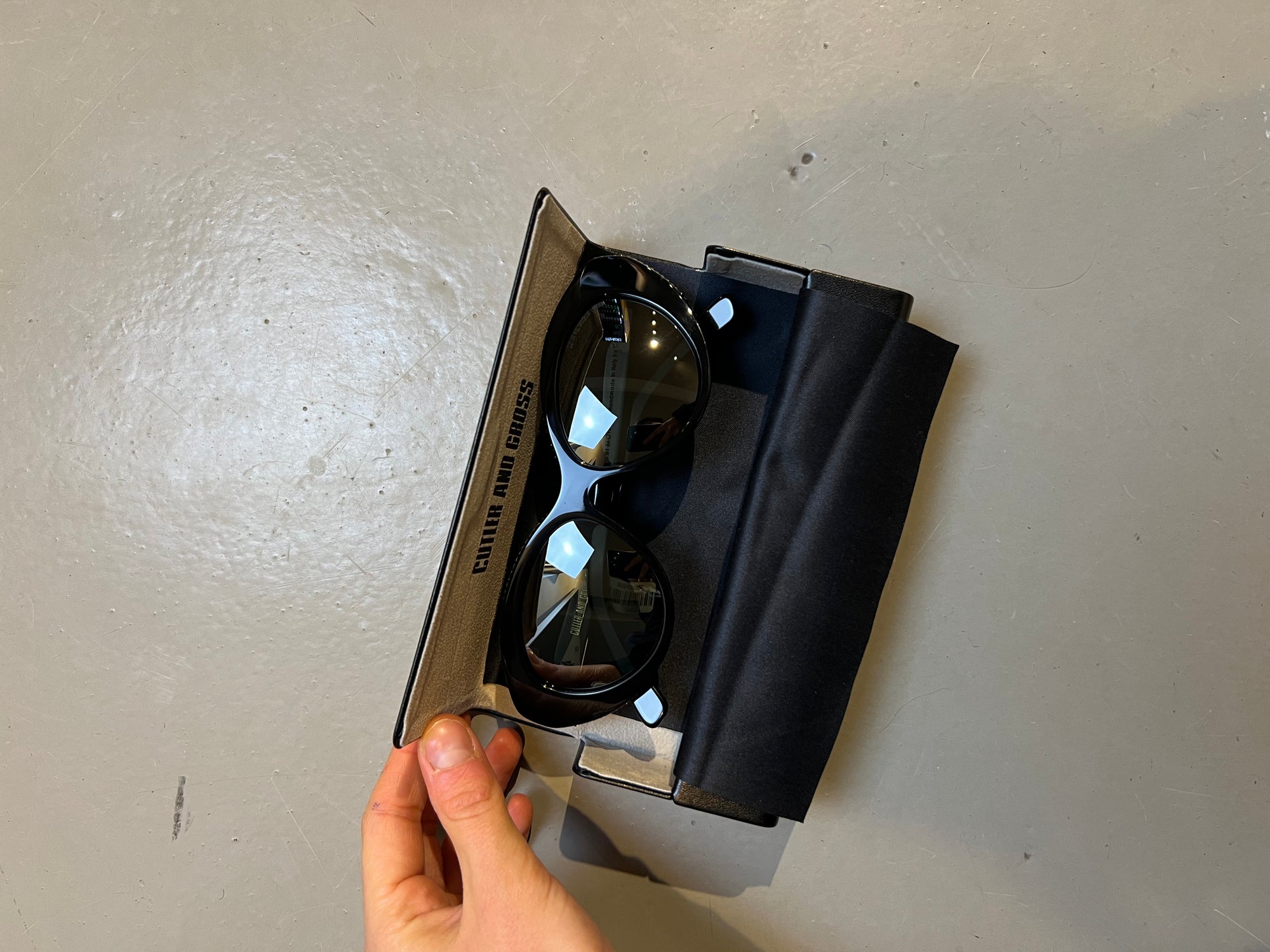 Produktbild der Cutler and Gross Sunglasses Black Glitter von oben mit Case vor grauem Hintergrund.