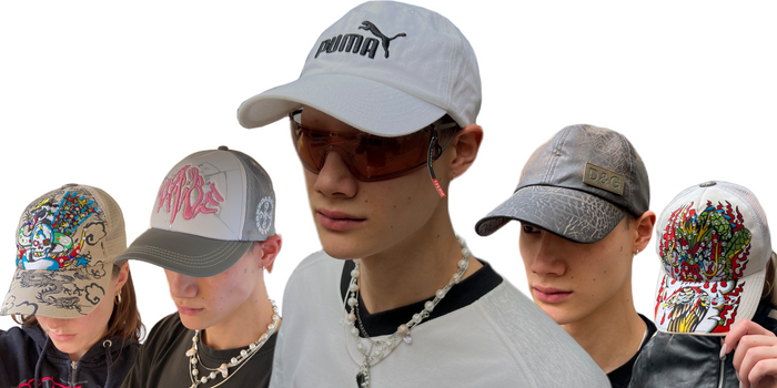 Zu sehen sind fünf Vintage Caps. Wie zum Beispiel eine weiße mit schwarzem Puma Logo, eine weiße Ed Hardy oder eine graue Dolce&Gabbana mit Ledermuster.