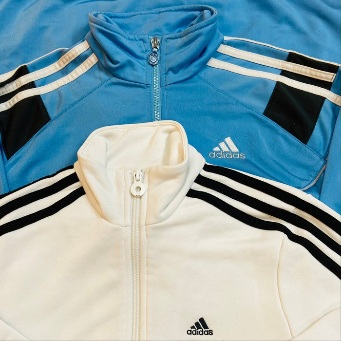 Zu sehen sind zwei Adidas Jacken, eine in Creme und eine in Blau.