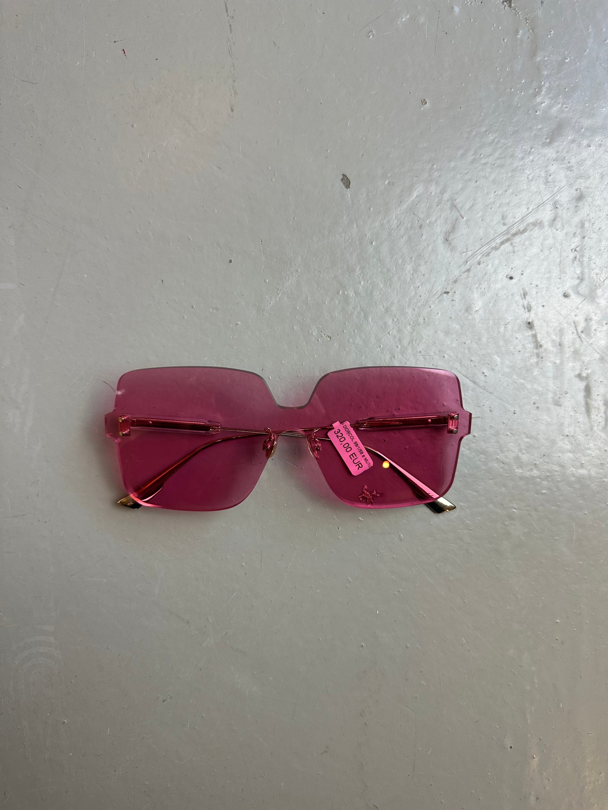 Produktbild von einer pinken Christian Dior Sonnenbrille ohne Rahmen vor grauem Hintergrund.