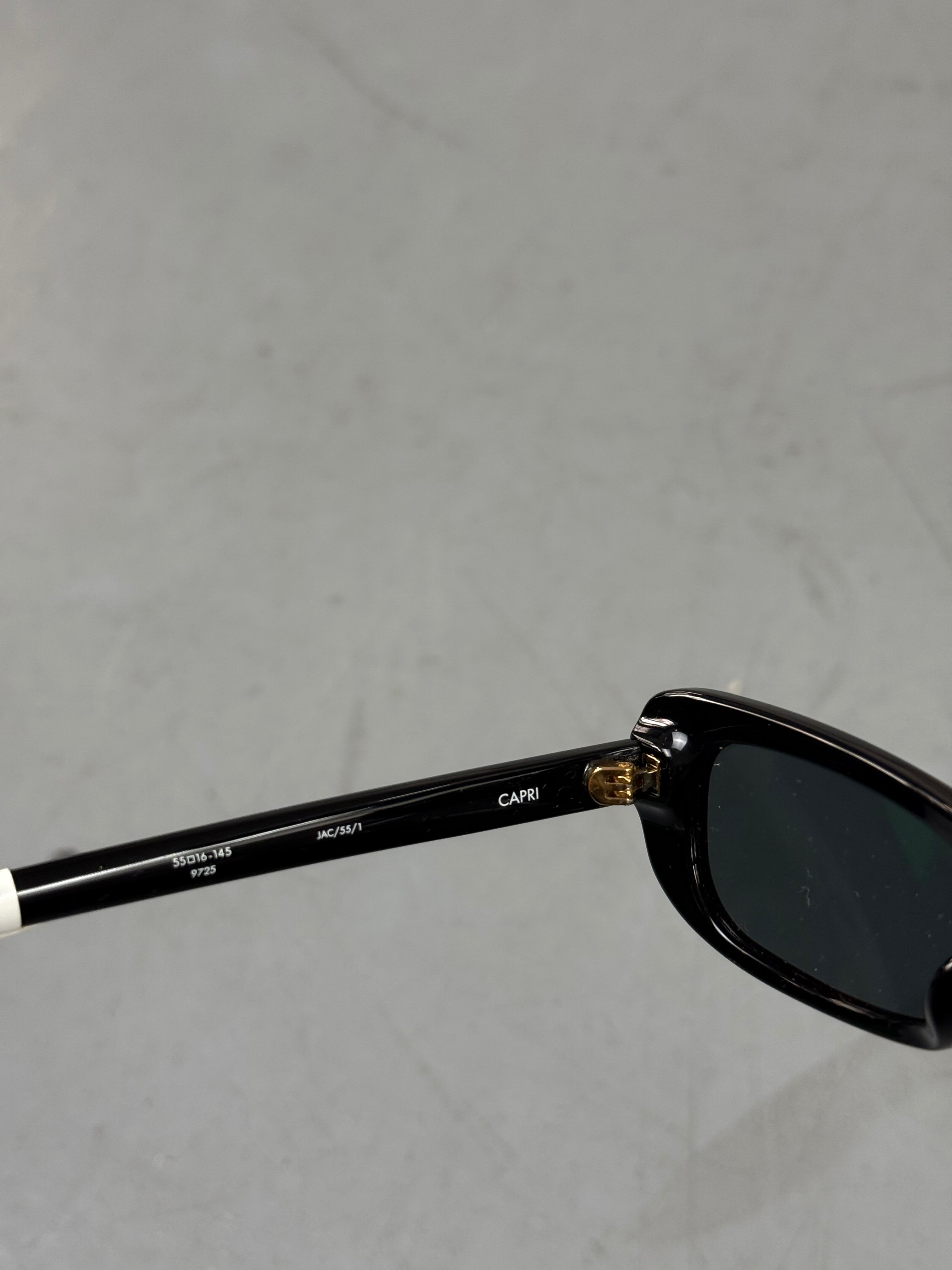 Eine schwarze schmale Sonnenbrille von Jacquemus mit goldenem Brand na,e auf den Bügeln 