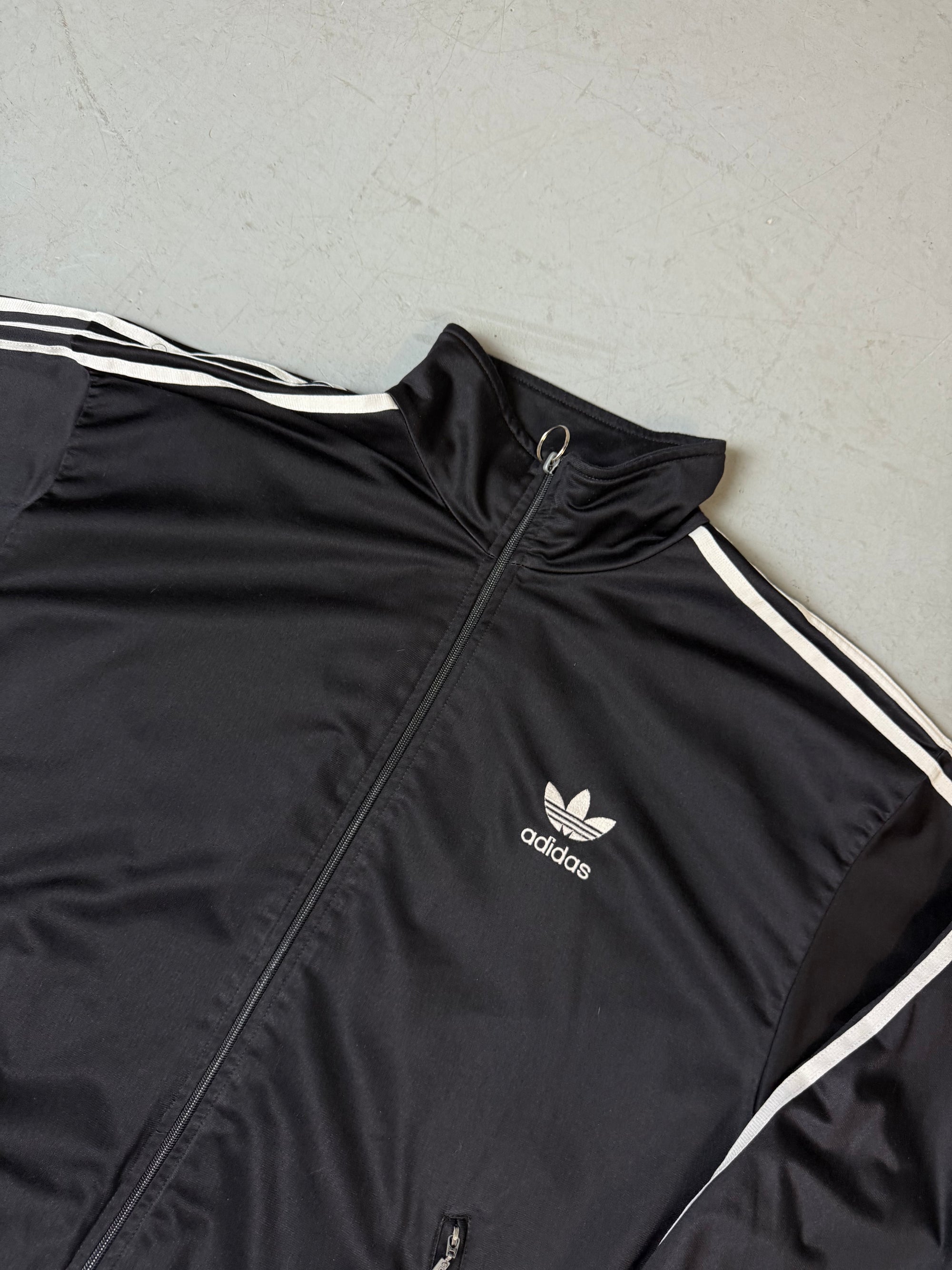 Eine schwarze vintage Adidas Track Jacke mit weißen Streifen und Firebird Logo 