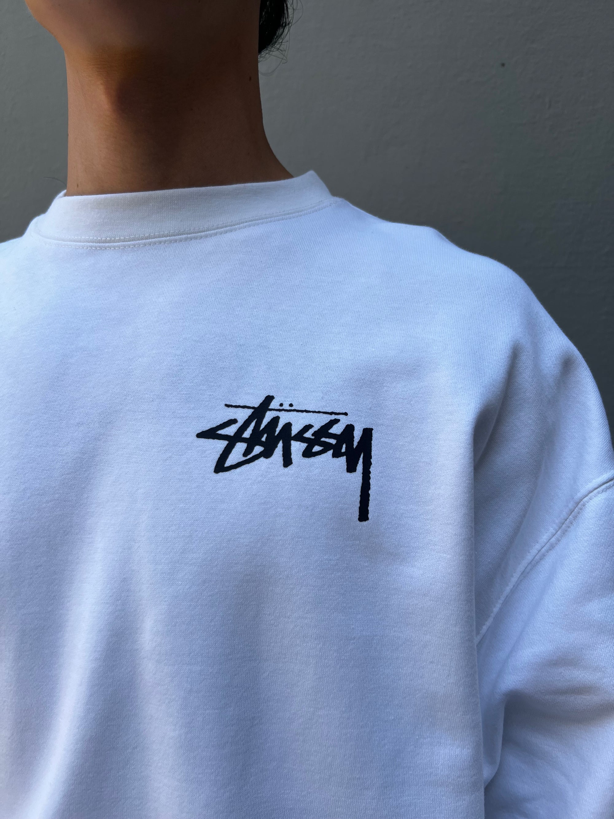 Close up Bild von Stüssy Logo Tragebild von vorne vor grauer Wand