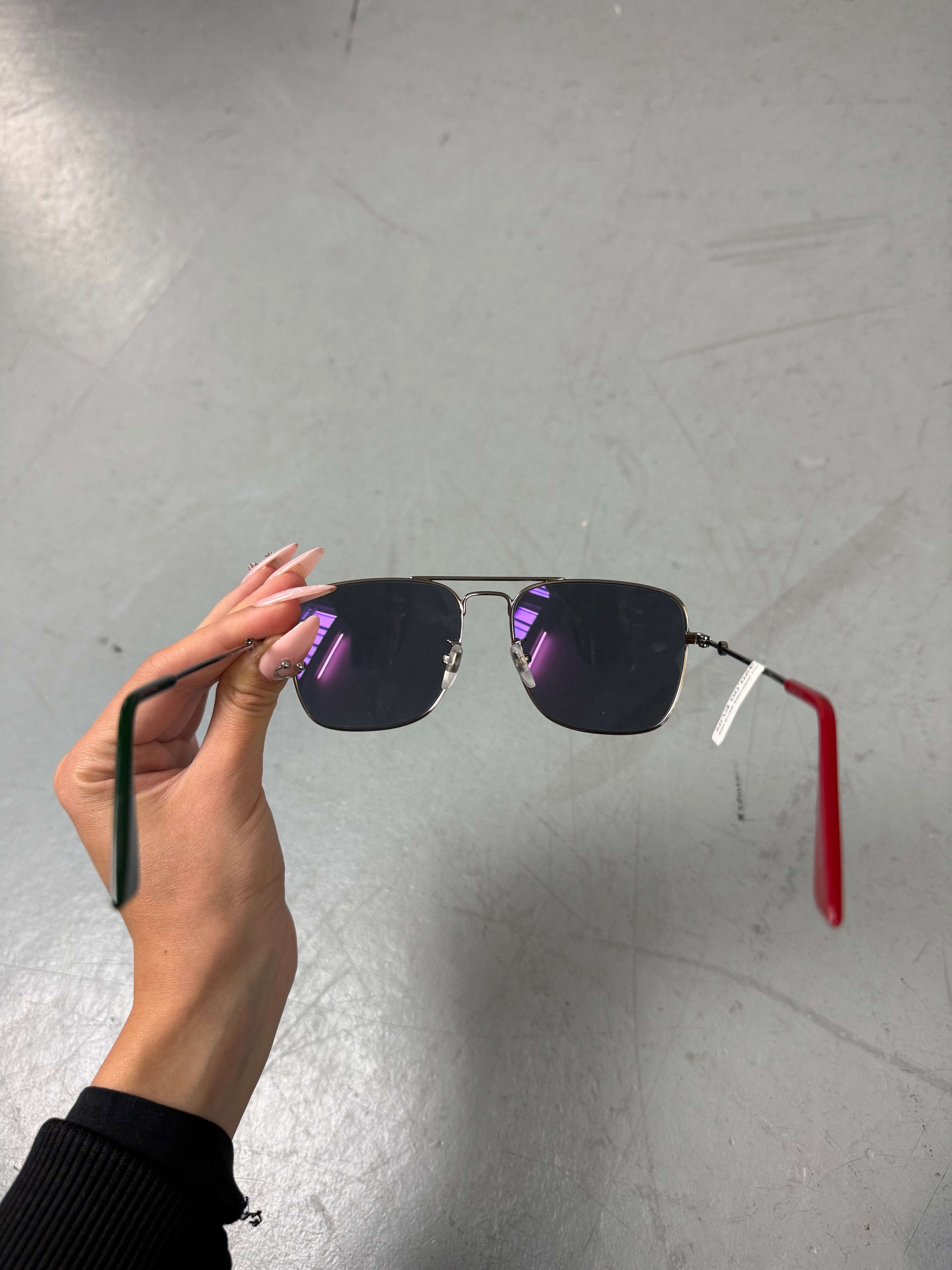 Eine eckige Sonnenbrille von gucci mit dunklen Gläsern und roten und grünen Elementen an den Bügeln 