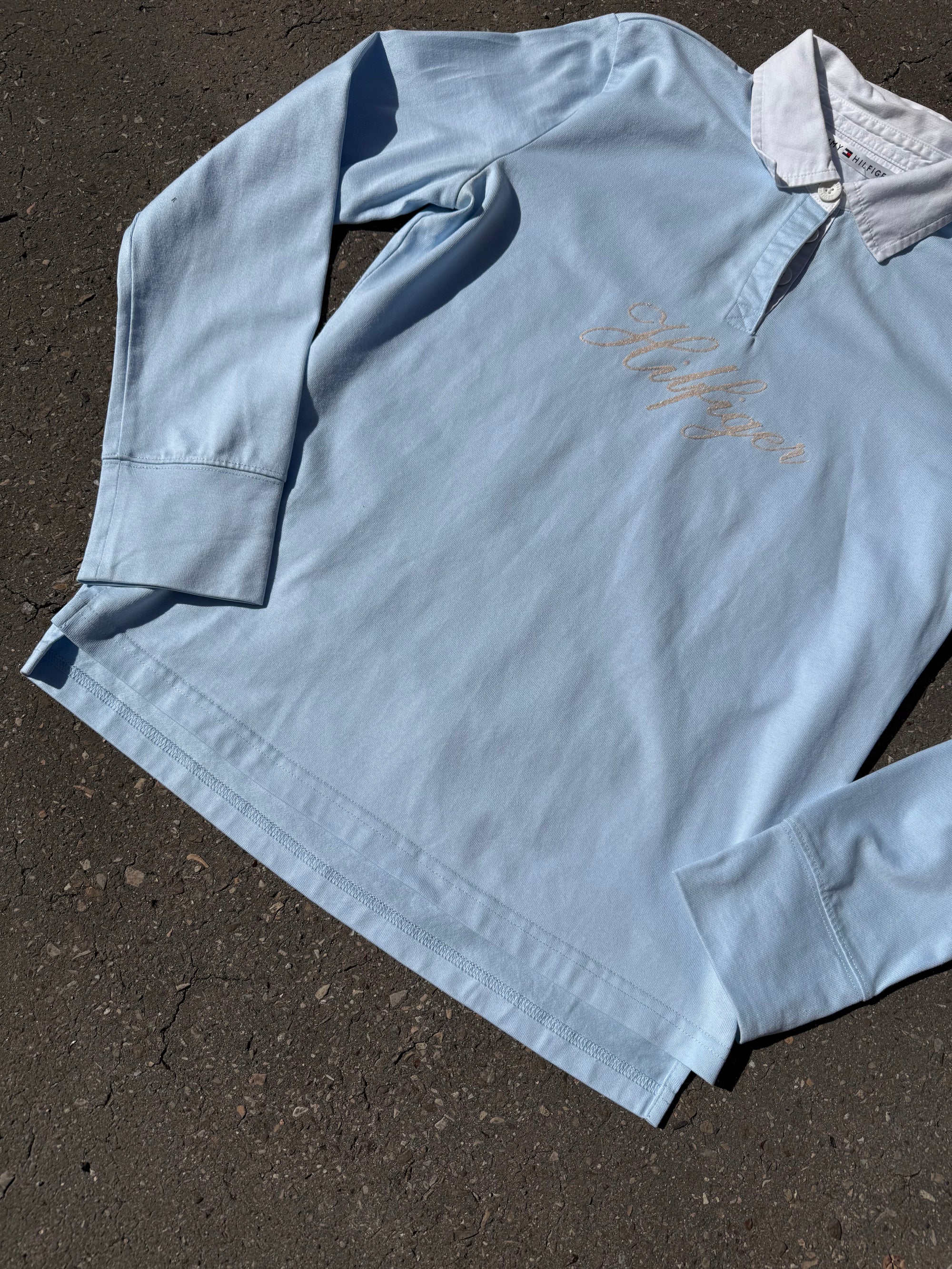 Ein babyblaues langärmliges Polo mit weißem Kragen und Hilfiger in Silber auf der Brust geschrieben 