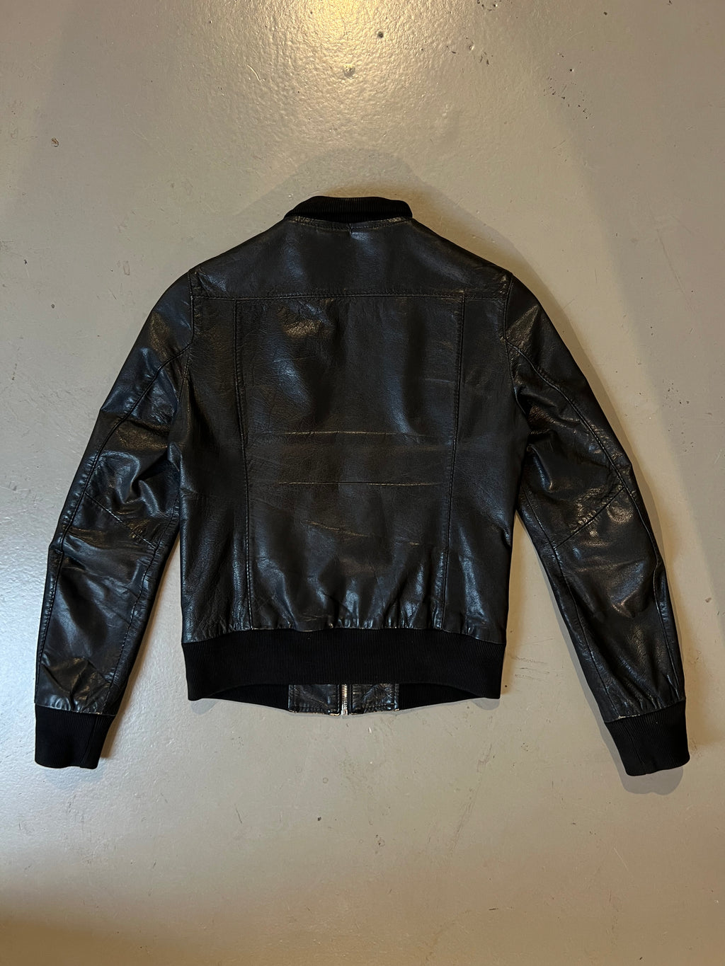 Produktbild von schwarzer Lederjacke auf grauem Boden hinten