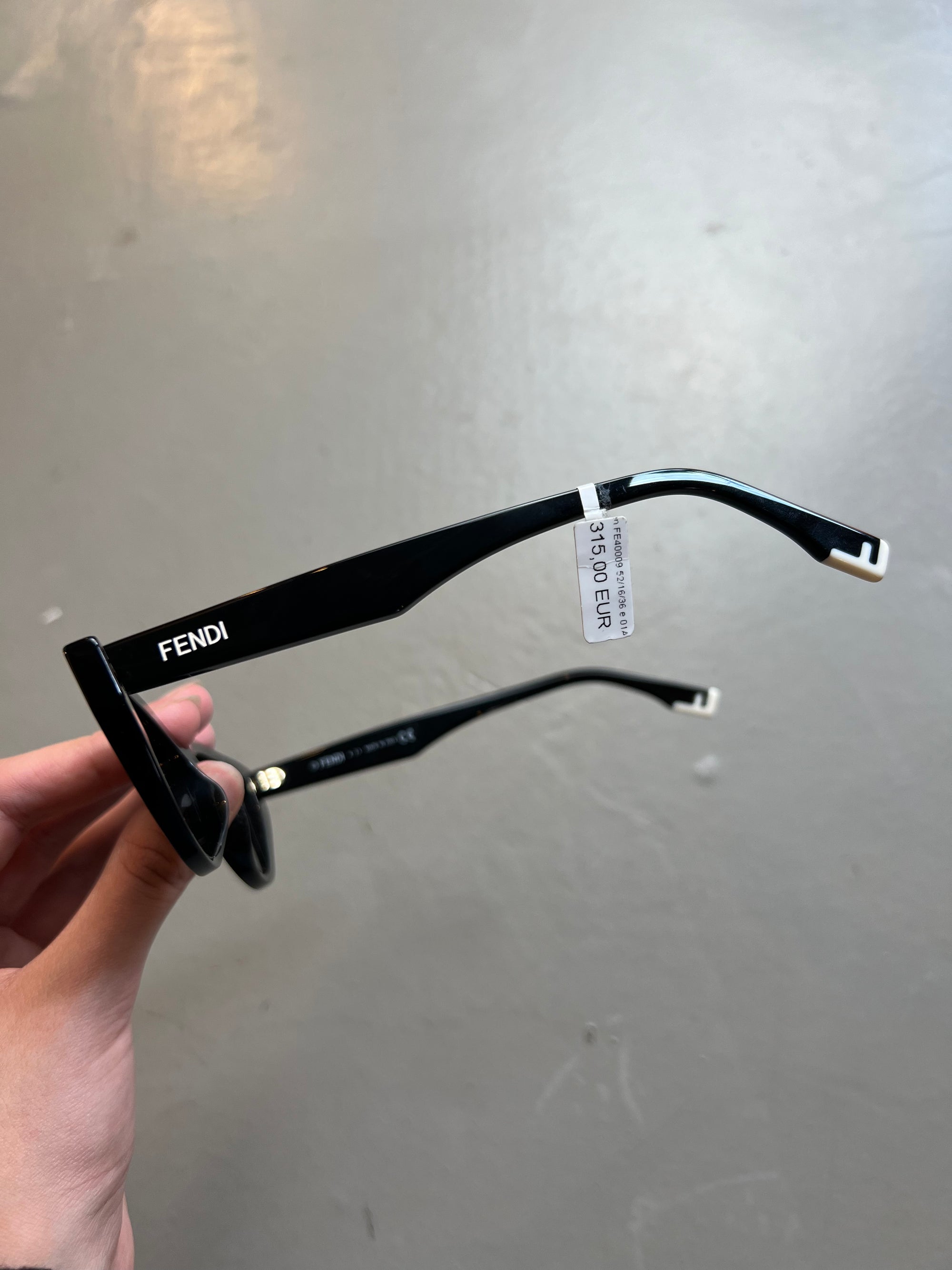 Detail-Produktbild von schwarzer Fendi Cat-Eye Sonnenbrille vor grauem Hintergrund.