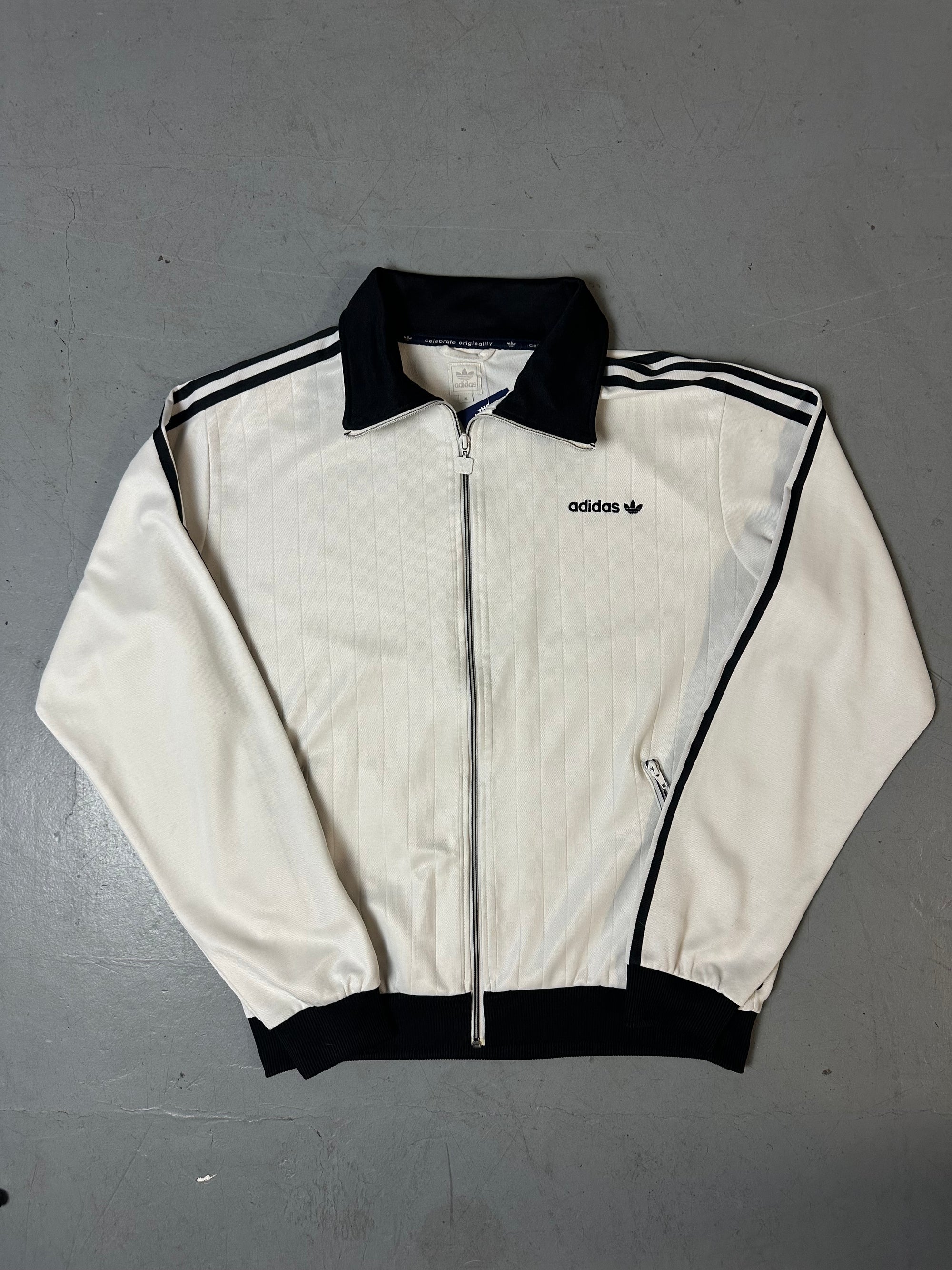Eine weiße Trackjacke von Adidas mit schwarzen Streifen, schwarzer Kragen und dem Logo in schwarz auf der Brust 
