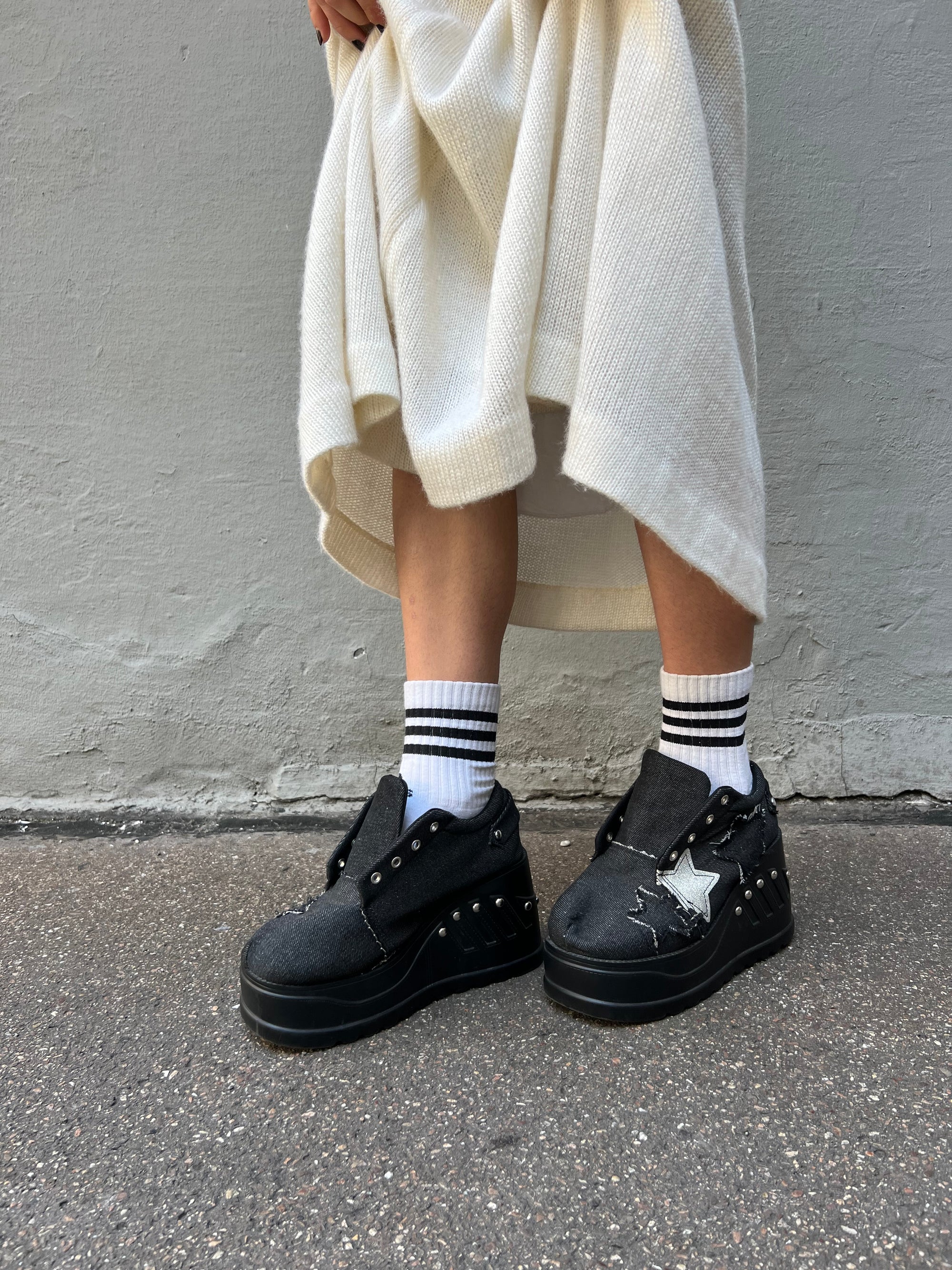 Schwarze denim sneaker mit Plateau Absatz und Sternen in schwarz und weiß. Tragebild vor grauem Hintergrund. Seitlich.
