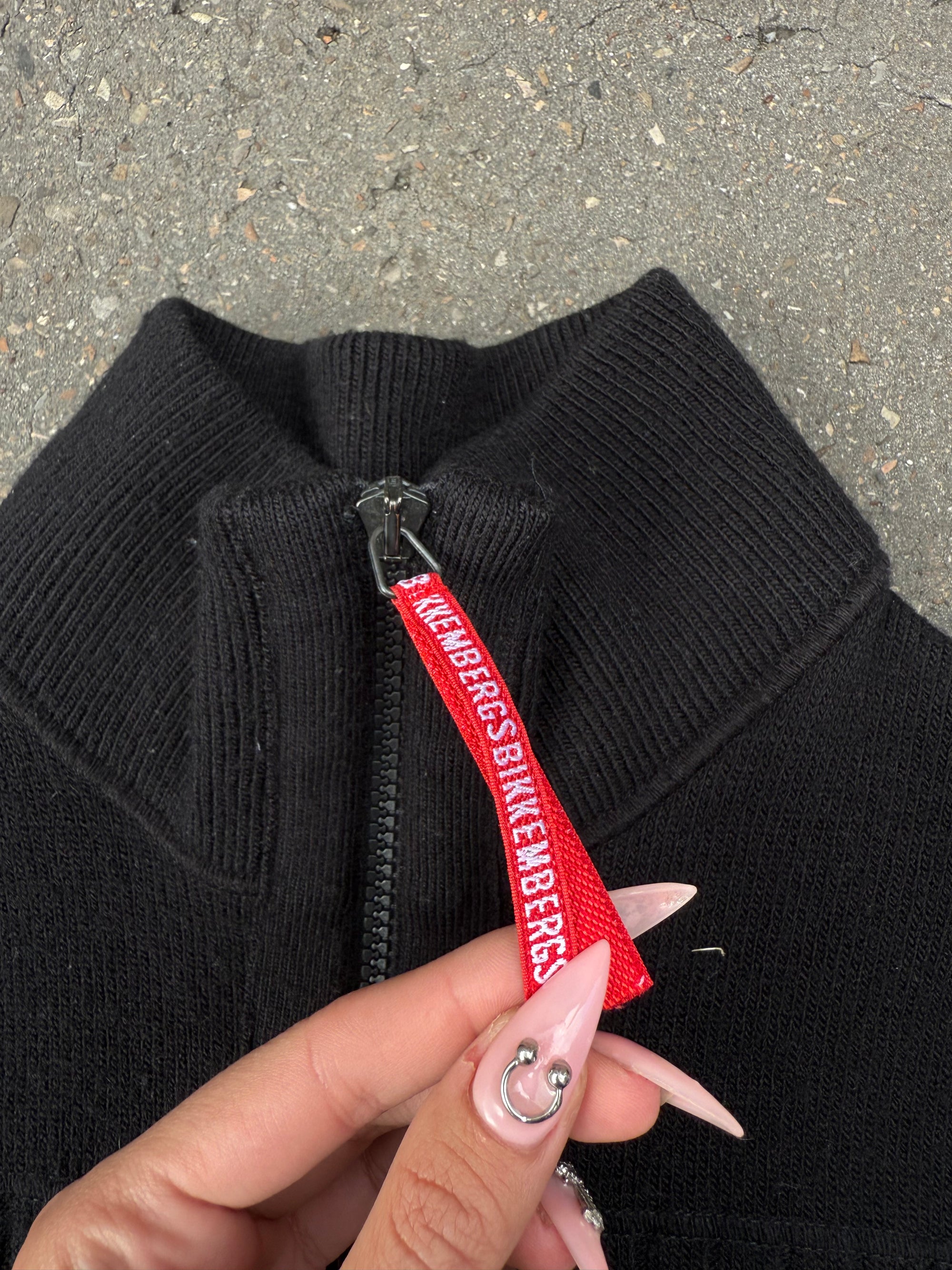 Ein schwarzer Strick Zipper von Dirk Bikkembergs mit roter Schlaufe am Reißverschluss in XS