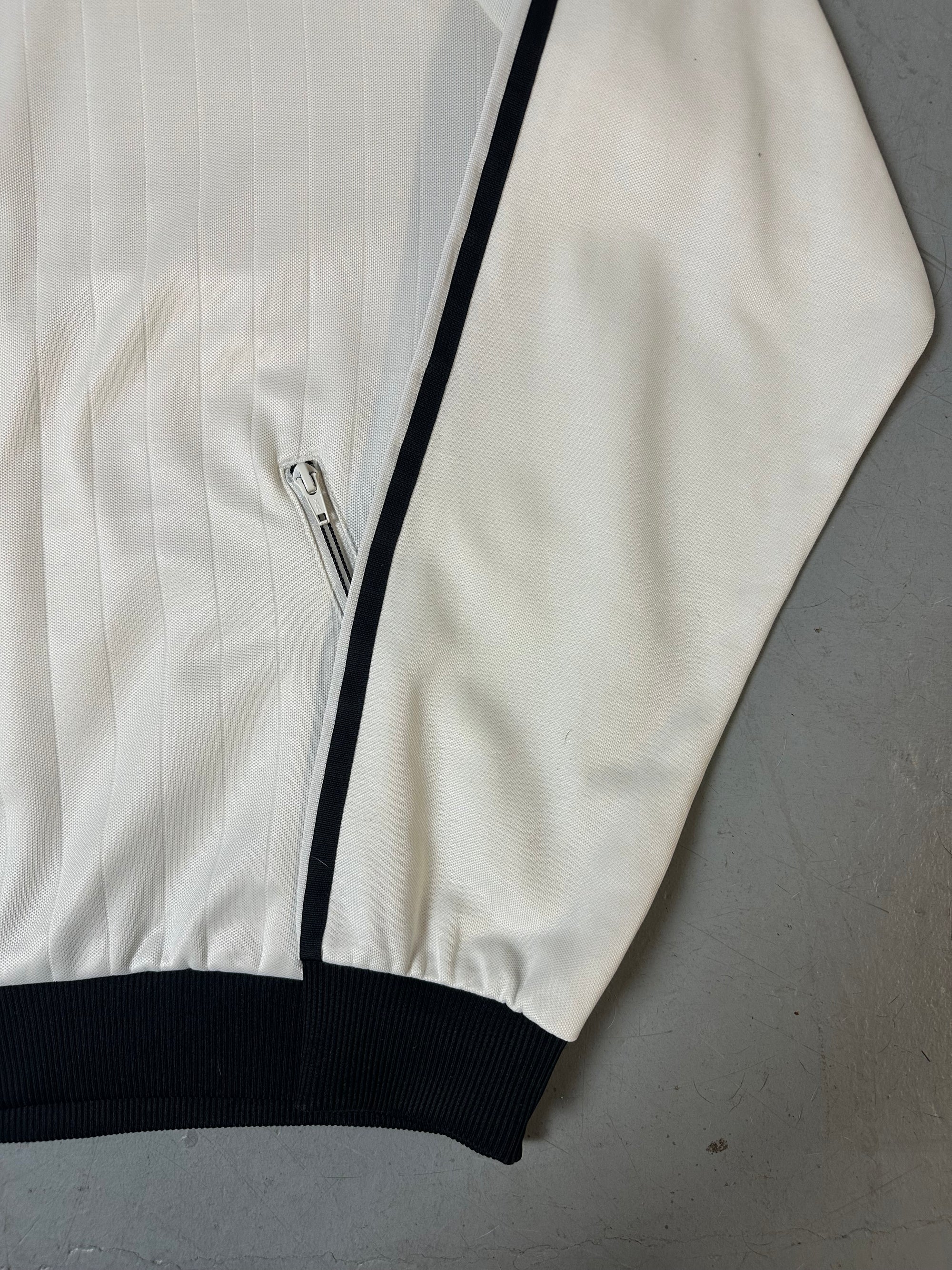 Eine weiße Trackjacke von Adidas mit schwarzen Streifen, schwarzer Kragen und dem Logo in schwarz auf der Brust 