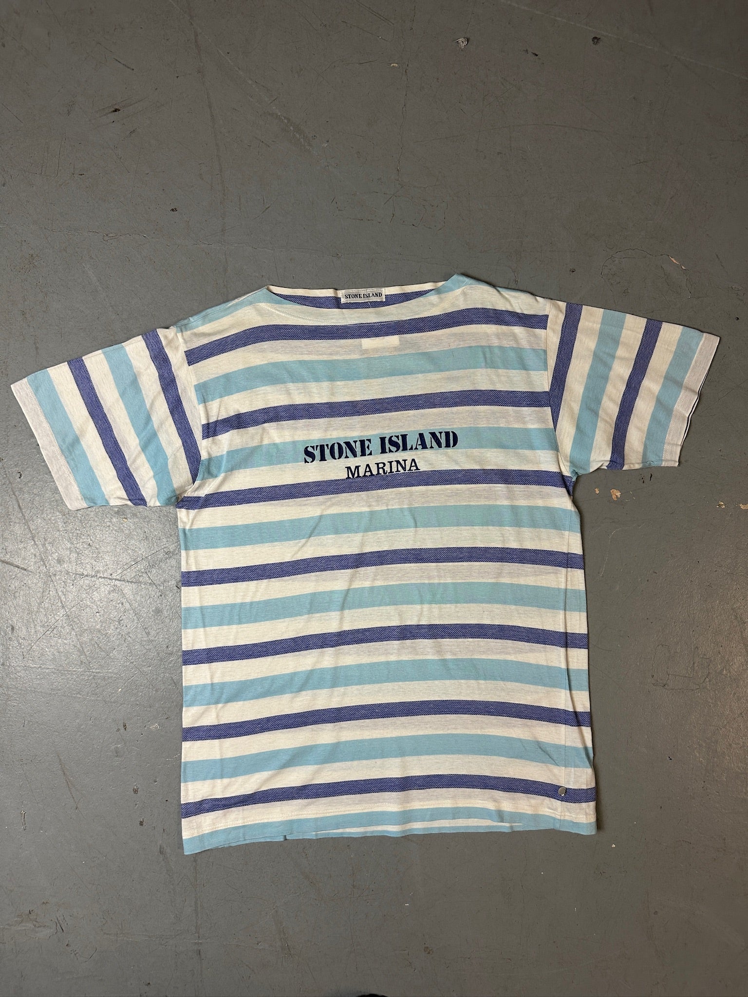 Produktbild von blau weis gestreiftem Stone Island Tshirt auf grauem Boden 