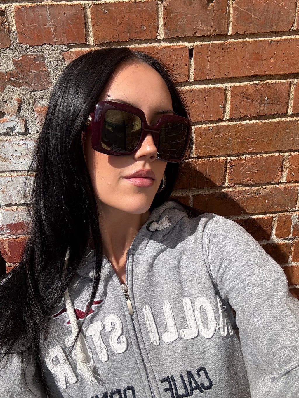 Eine burgunderrote Sonnenbrille von Gucci mit dem Logo in Gold an der Seite und großen quadratischen Gläsern