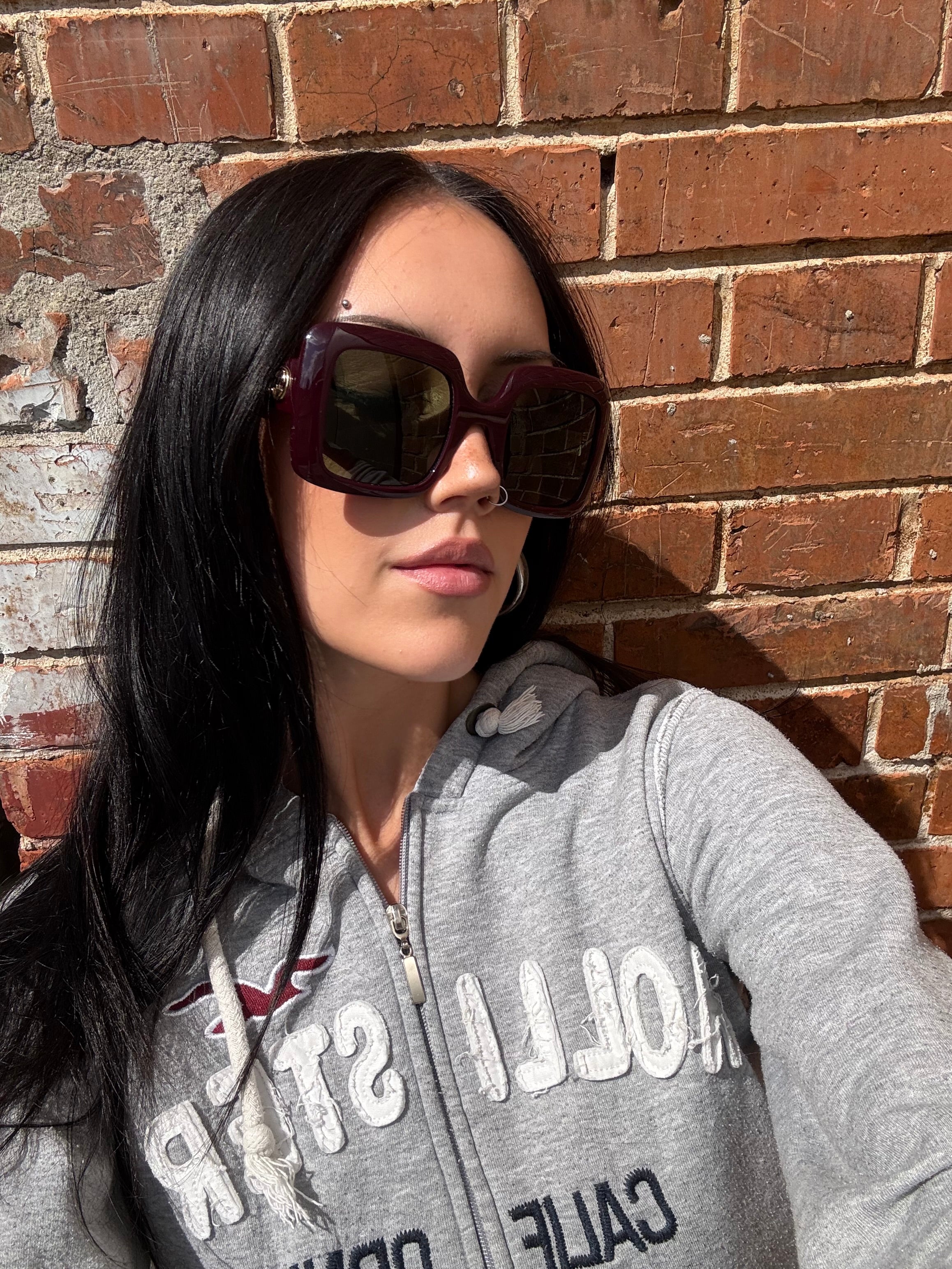 Eine burgunderrote Sonnenbrille von Gucci mit dem Logo in Gold an der Seite und großen quadratischen Gläsern