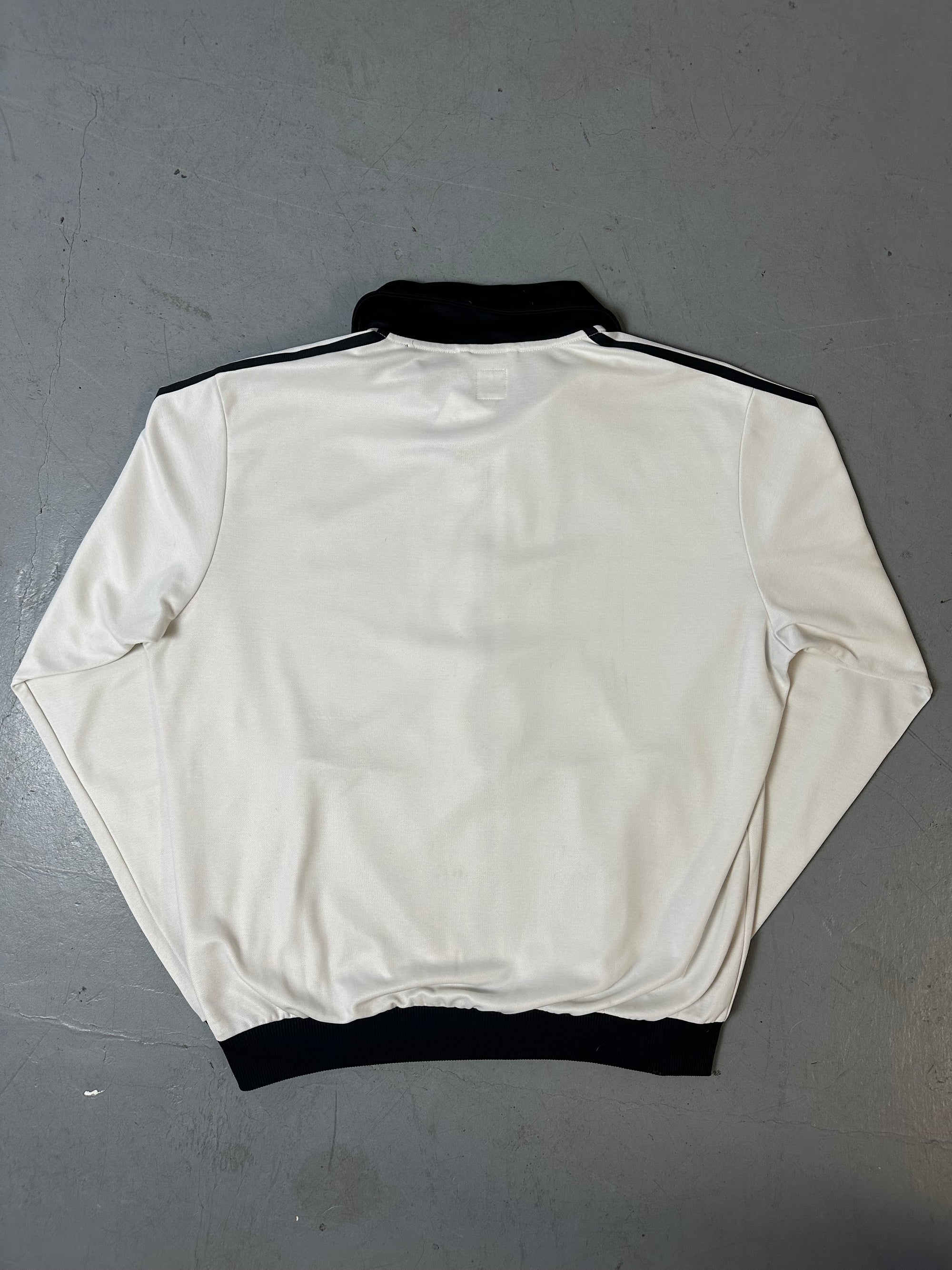 Eine weiße Trackjacke von Adidas mit schwarzen Streifen, schwarzer Kragen und dem Logo in schwarz auf der Brust 