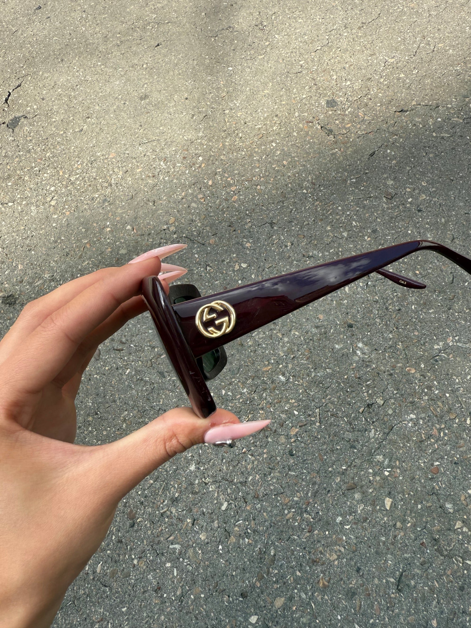 Eine burgunderrote Sonnenbrille von Gucci mit dem Logo in Gold an der Seite und großen quadratischen Gläsern
