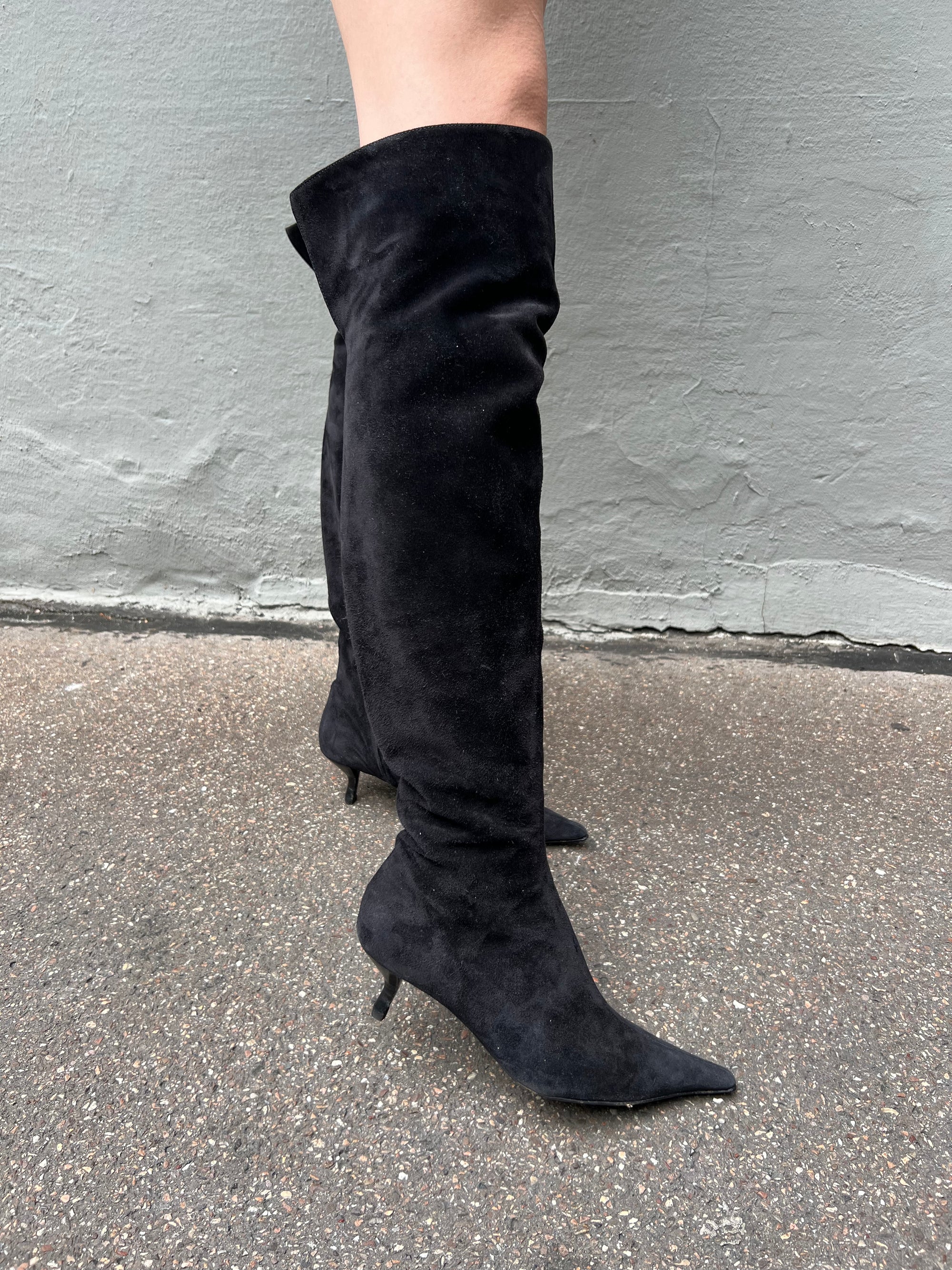 Zu sehen sind kniehohe schwarze Stiefel mit dünnen Absätzen von Fendi in Größe 38,5 von der Seite vor einem grauen Hintergrund.