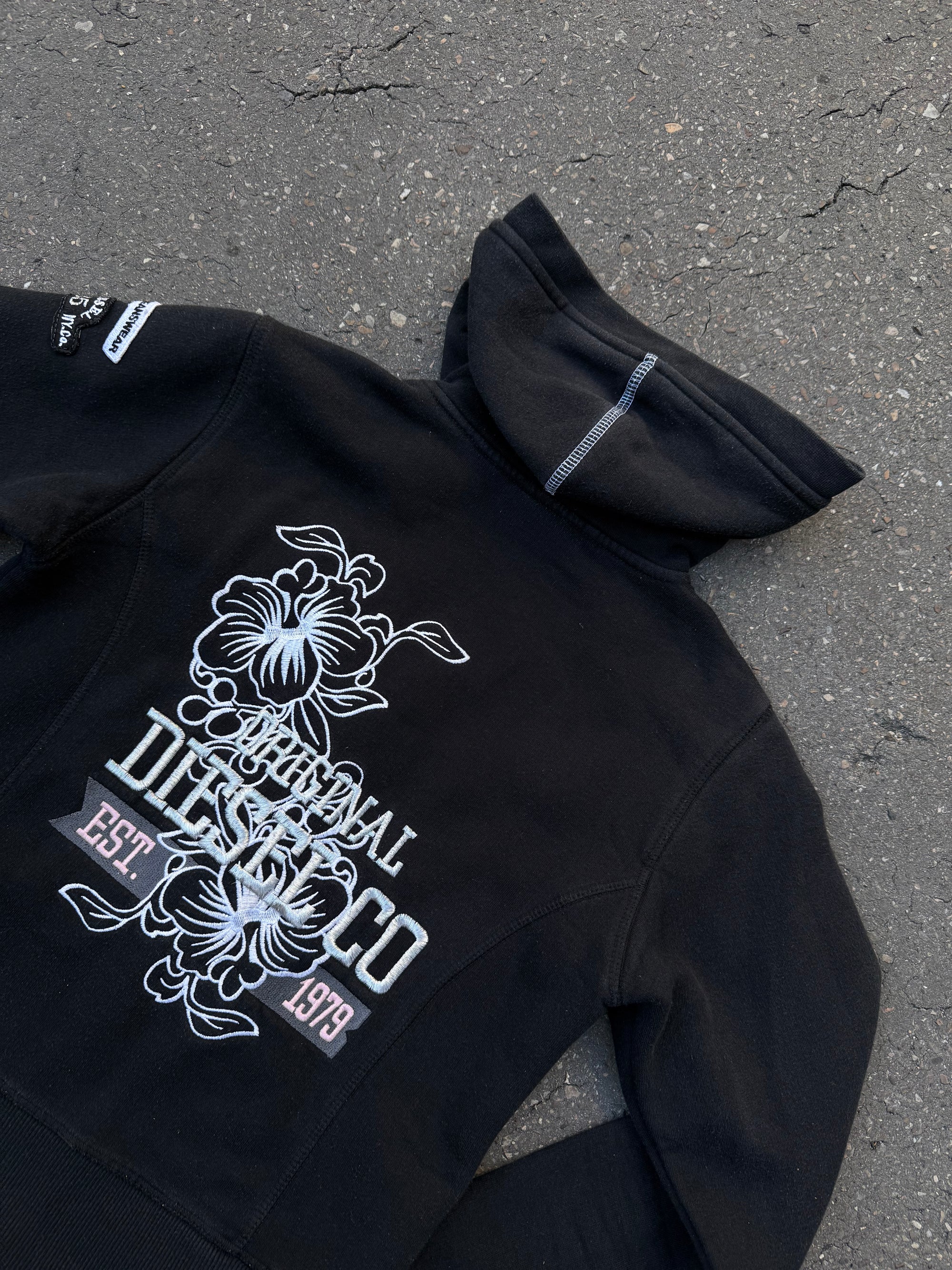 Ein schwarzer Zip Up Hoodie von Diesel mit dem Logo in weiß auf der Vorderseite und einem weißen Print auf der Rückseite