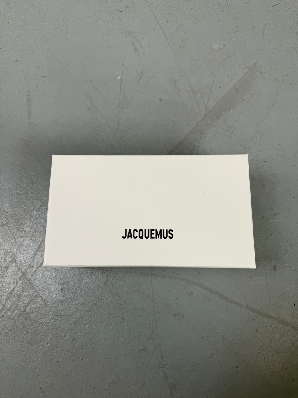Eine schwarze schmale Sonnenbrille von Jacquemus mit goldenem Brand na,e auf den Bügeln 