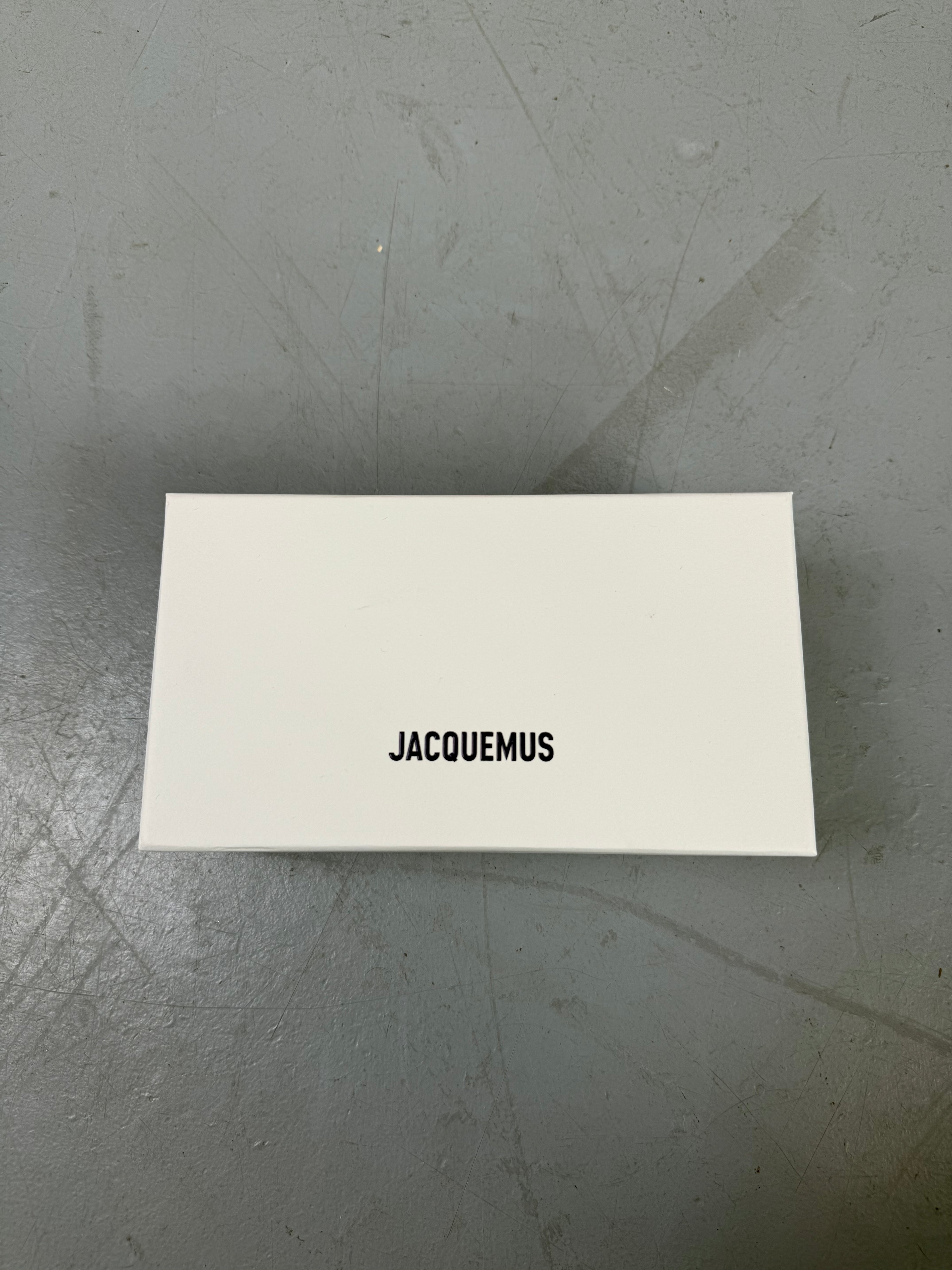 Eine schwarze schmale Sonnenbrille von Jacquemus mit goldenem Brand na,e auf den Bügeln 