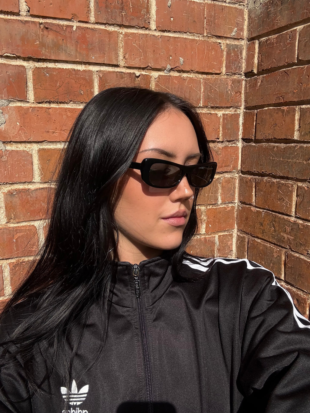 Eine schwarze schmale Sonnenbrille von Jacquemus mit goldenem Brand na,e auf den Bügeln 