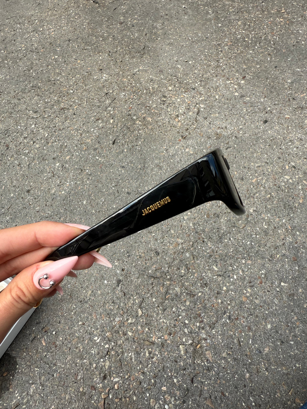 Eine schwarze Sonnenbrille von Jacquemus mit goldenem Schriftzug auf der Seite