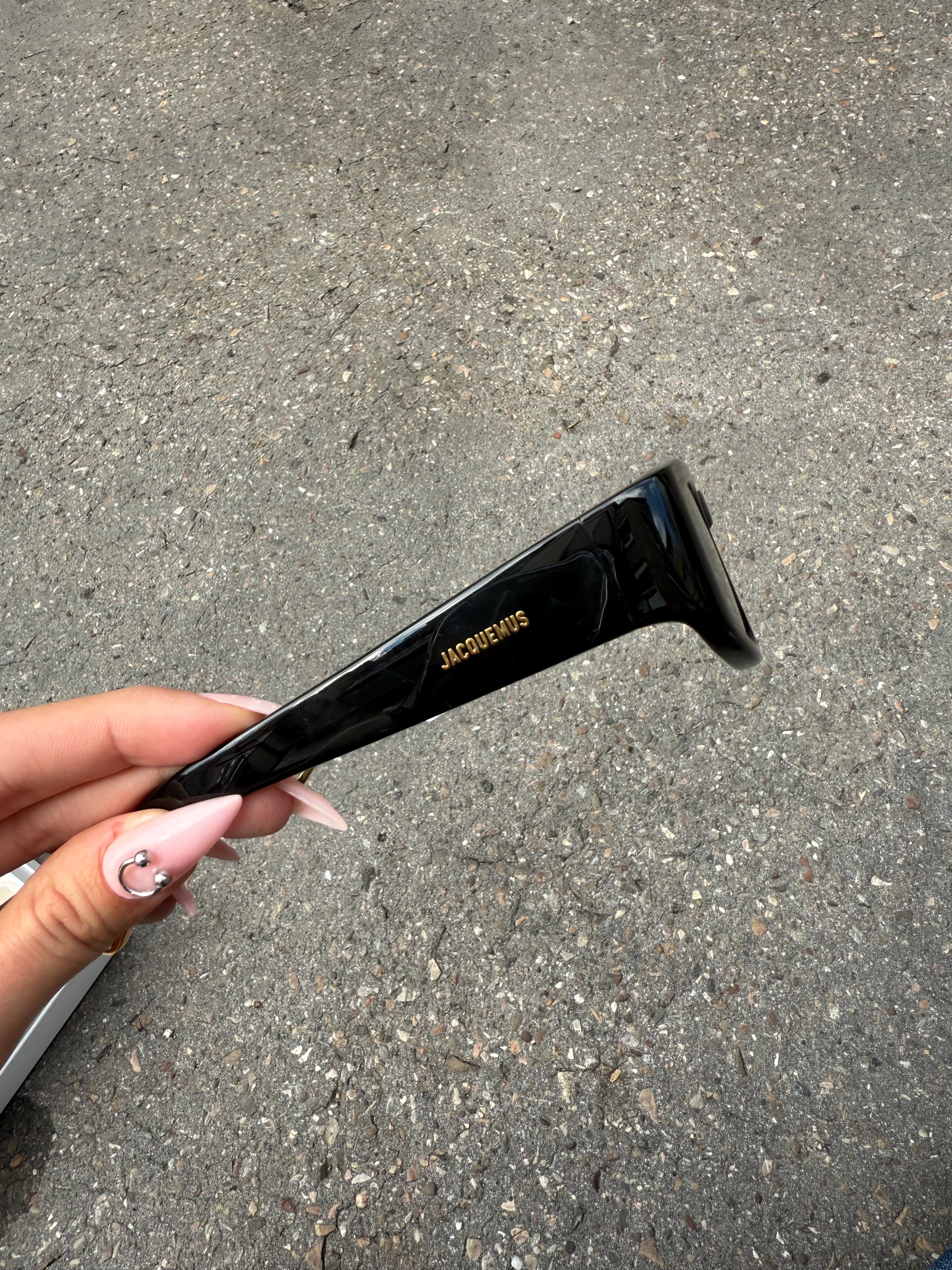 Eine schwarze Sonnenbrille von Jacquemus mit goldenem Schriftzug auf der Seite