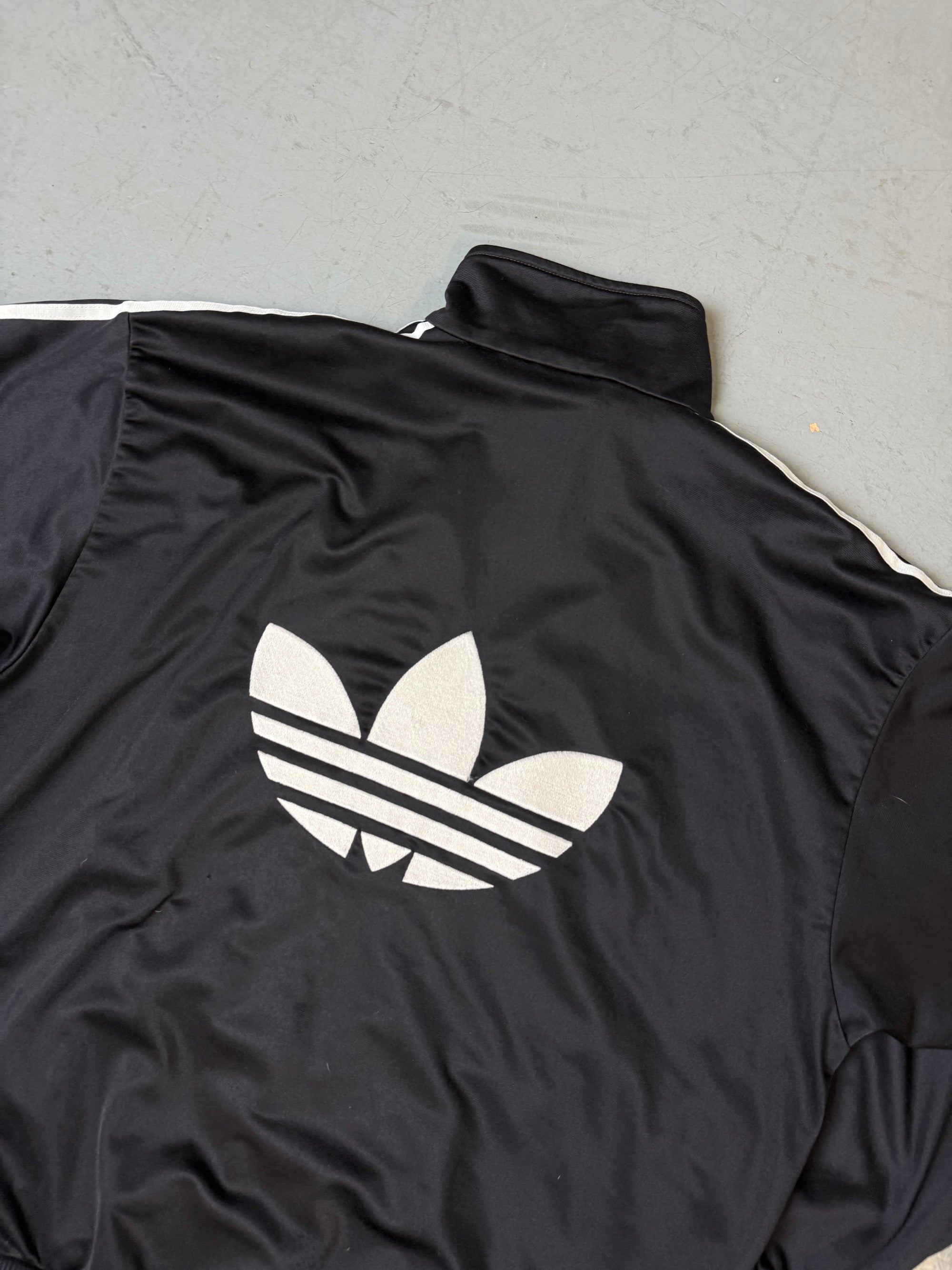 Eine schwarze vintage Adidas Track Jacke mit weißen Streifen und Firebird Logo 