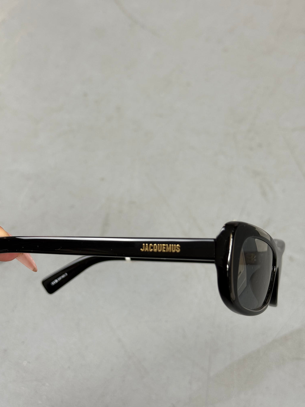 Eine schwarze schmale Sonnenbrille von Jacquemus mit goldenem Brand na,e auf den Bügeln 