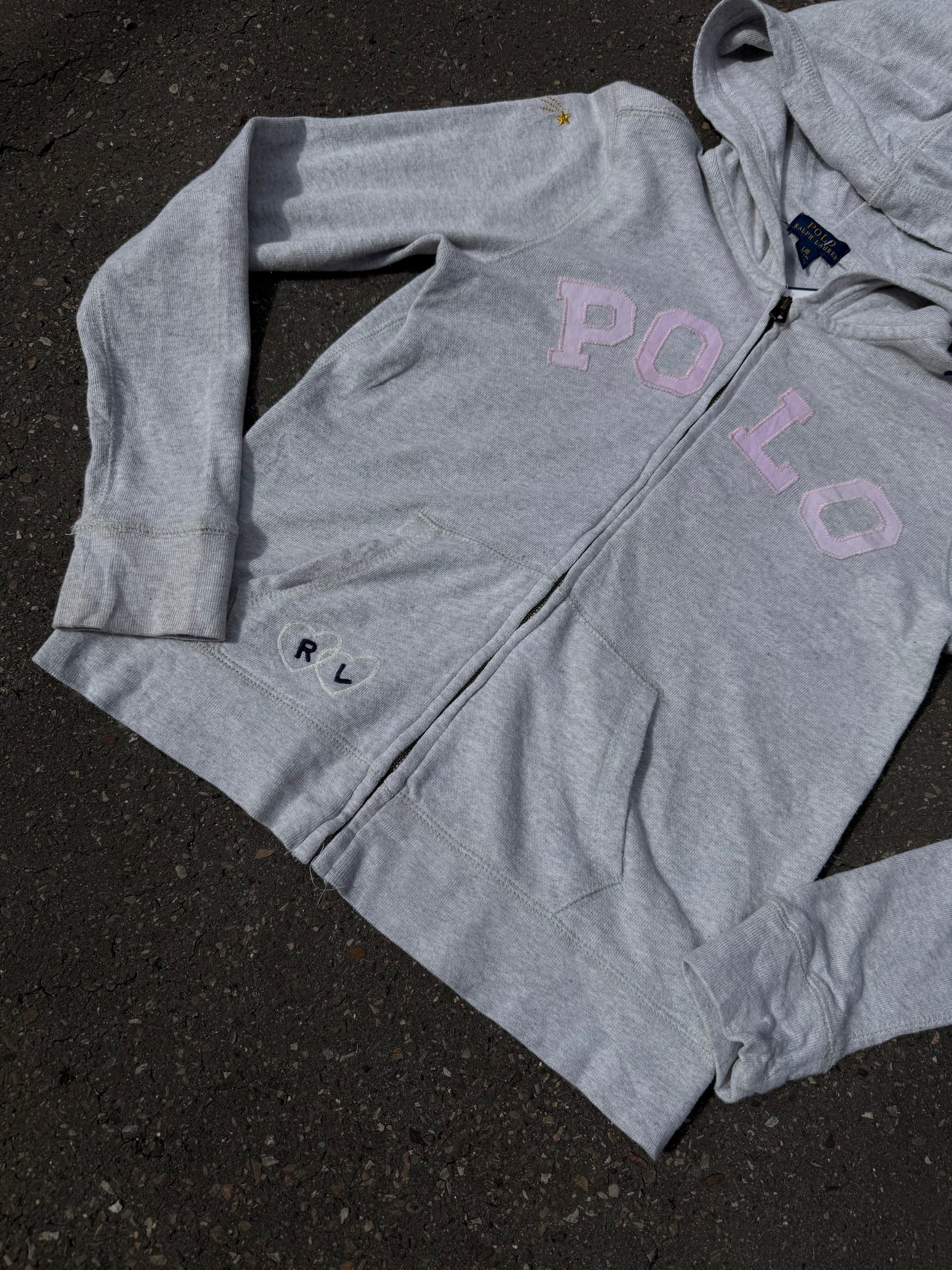 Ein grauer Zip Up Hoodie von Polo Ralph Lauren mit rosa Polo Aufdruck auf der Brust und kleinen patches überall verteilt in XS