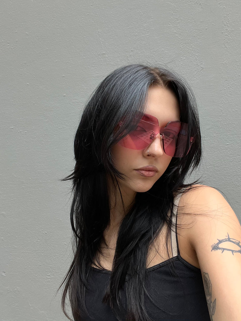 Tragebild von einer pinken Christian Dior Sonnenbrille ohne Rahmen vor grauem Hintergrund.
