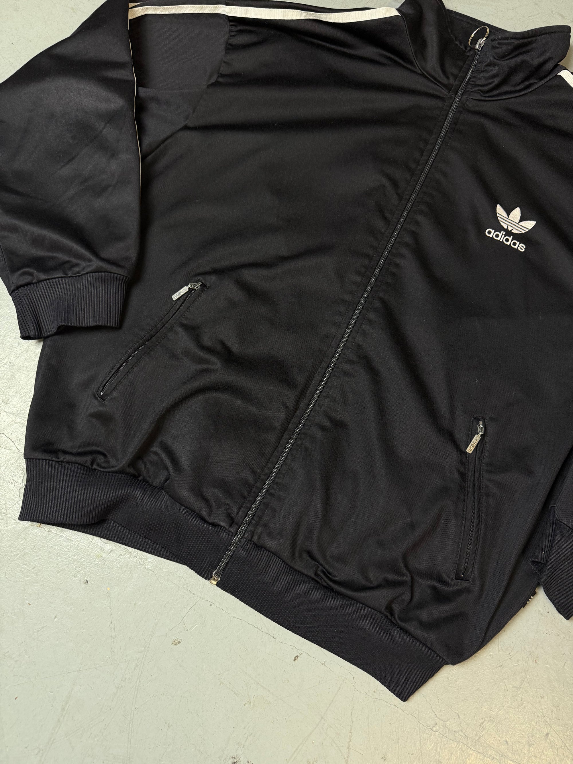 Eine schwarze vintage Adidas Track Jacke mit weißen Streifen und Firebird Logo 