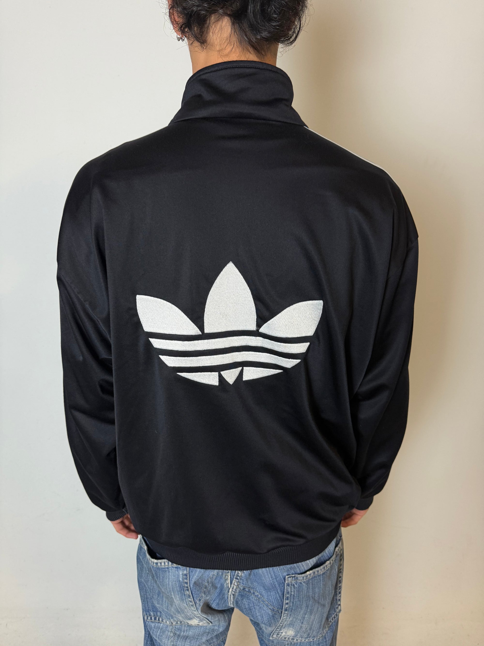 Eine schwarze vintage Adidas Track Jacke mit weißen Streifen und Firebird Logo 