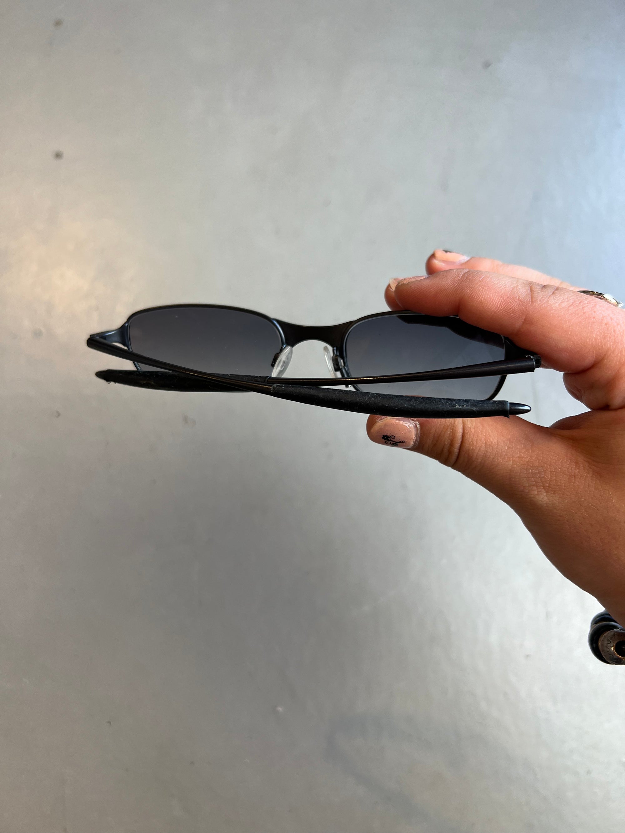 Auf dem Bild ist ein Produktbild der Oakley Raver Sunglasses in Schwarz von hinten vor einem grauem Hintergrund zu sehen.