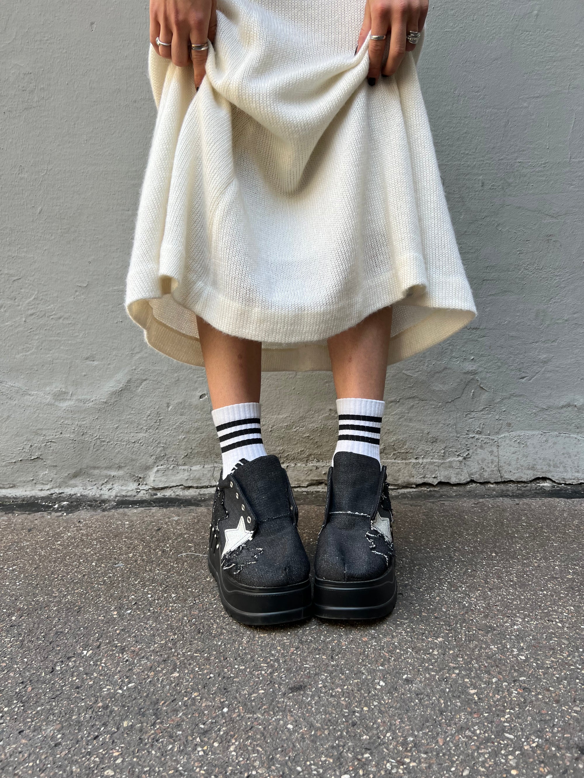 Schwarze denim sneaker mit Plateau Absatz und Sternen in schwarz und weiß. Tragebild vor grauem Hintergrund. Frontal. 