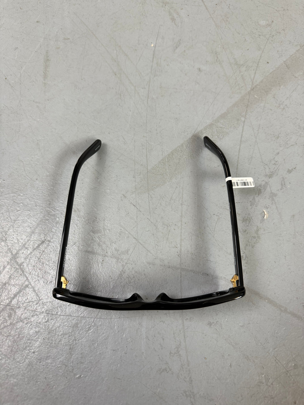 Eine schwarze schmale Sonnenbrille von Jacquemus mit goldenem Brand na,e auf den Bügeln 