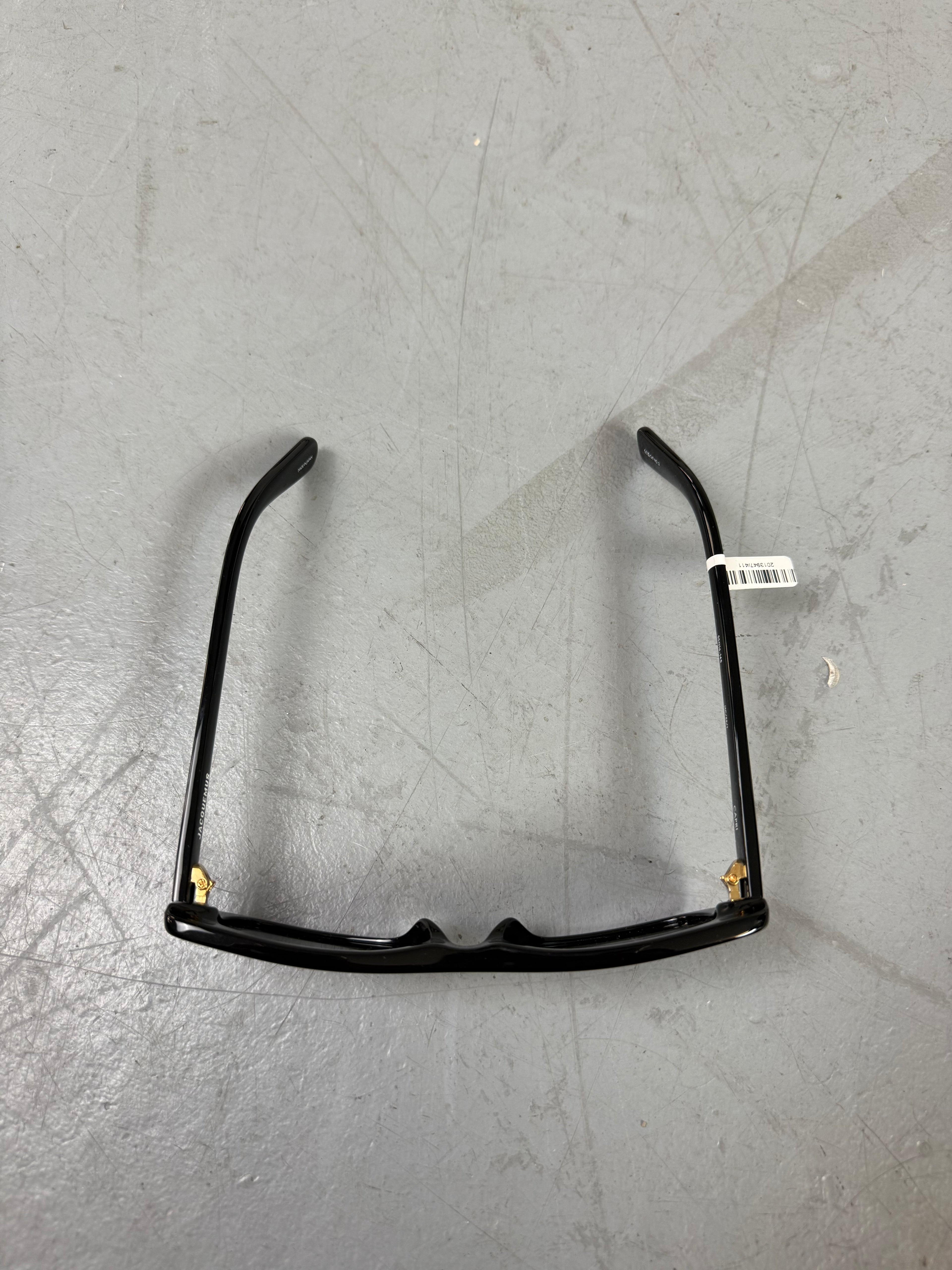 Eine schwarze schmale Sonnenbrille von Jacquemus mit goldenem Brand na,e auf den Bügeln 