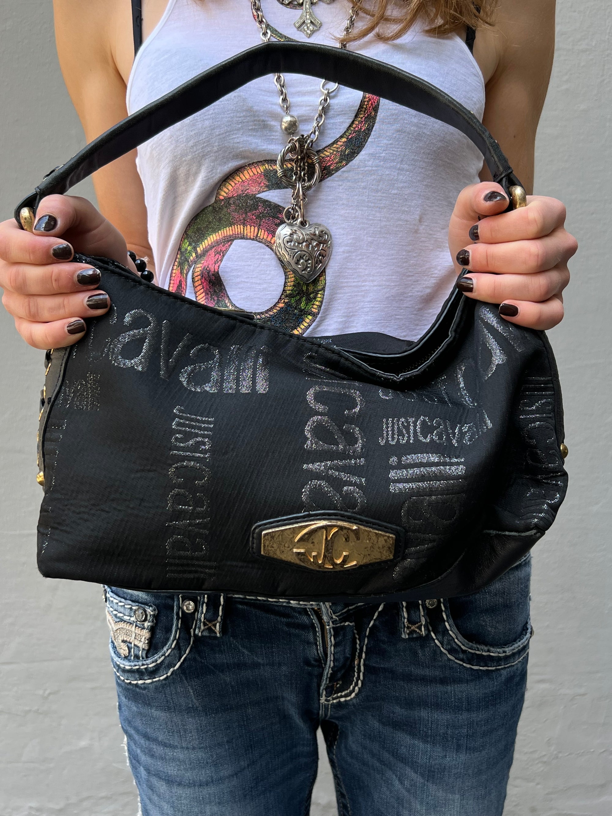 Schwarze schultertasche von just cavalli. Goldene Hardware, Monogramm Muster. Tragebild vir grauem Hintergrund. Vor dem Körper.