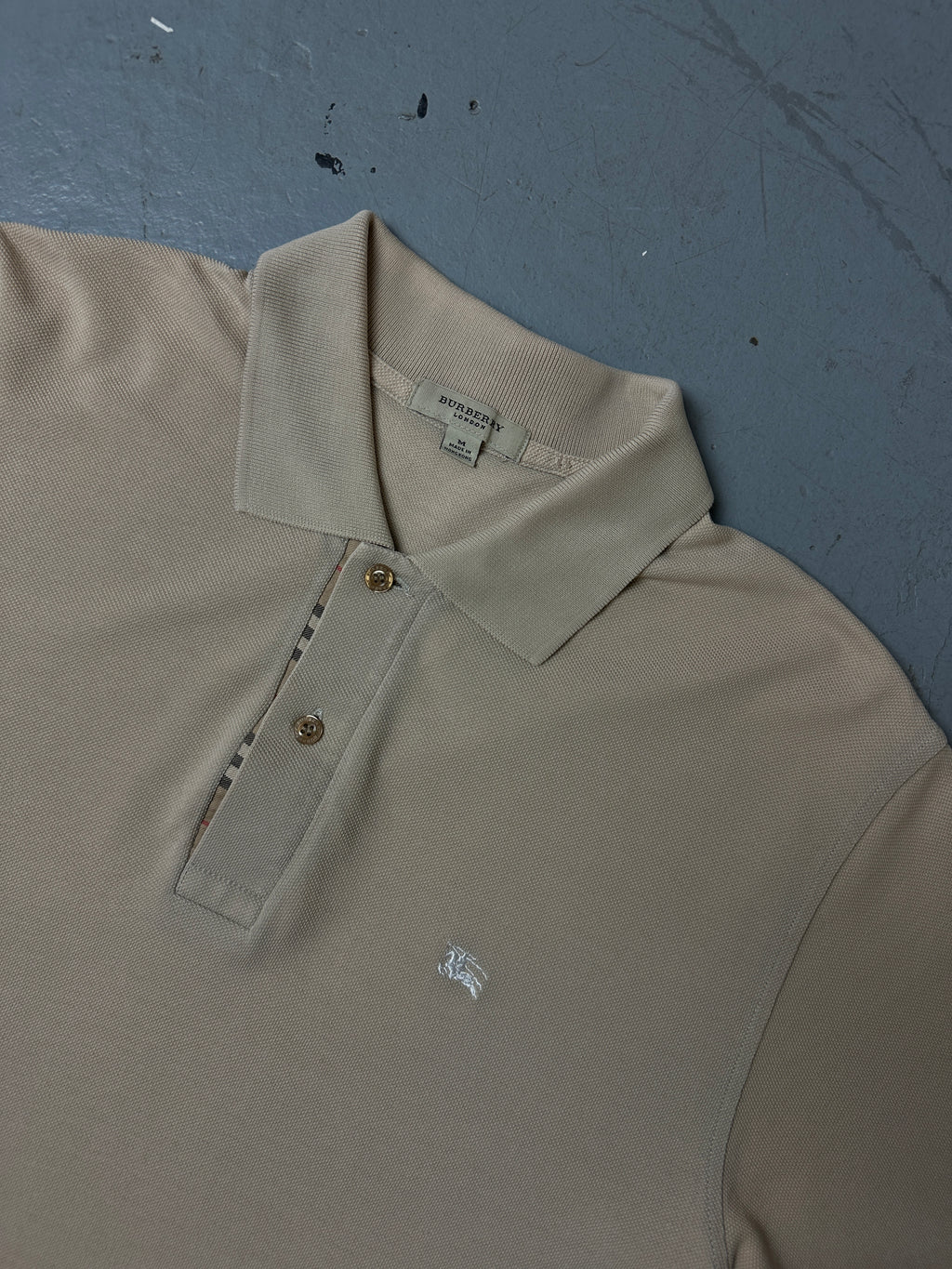 Detailliertes Produktbild von beigenen Burberry Polo auf grauem Boden 