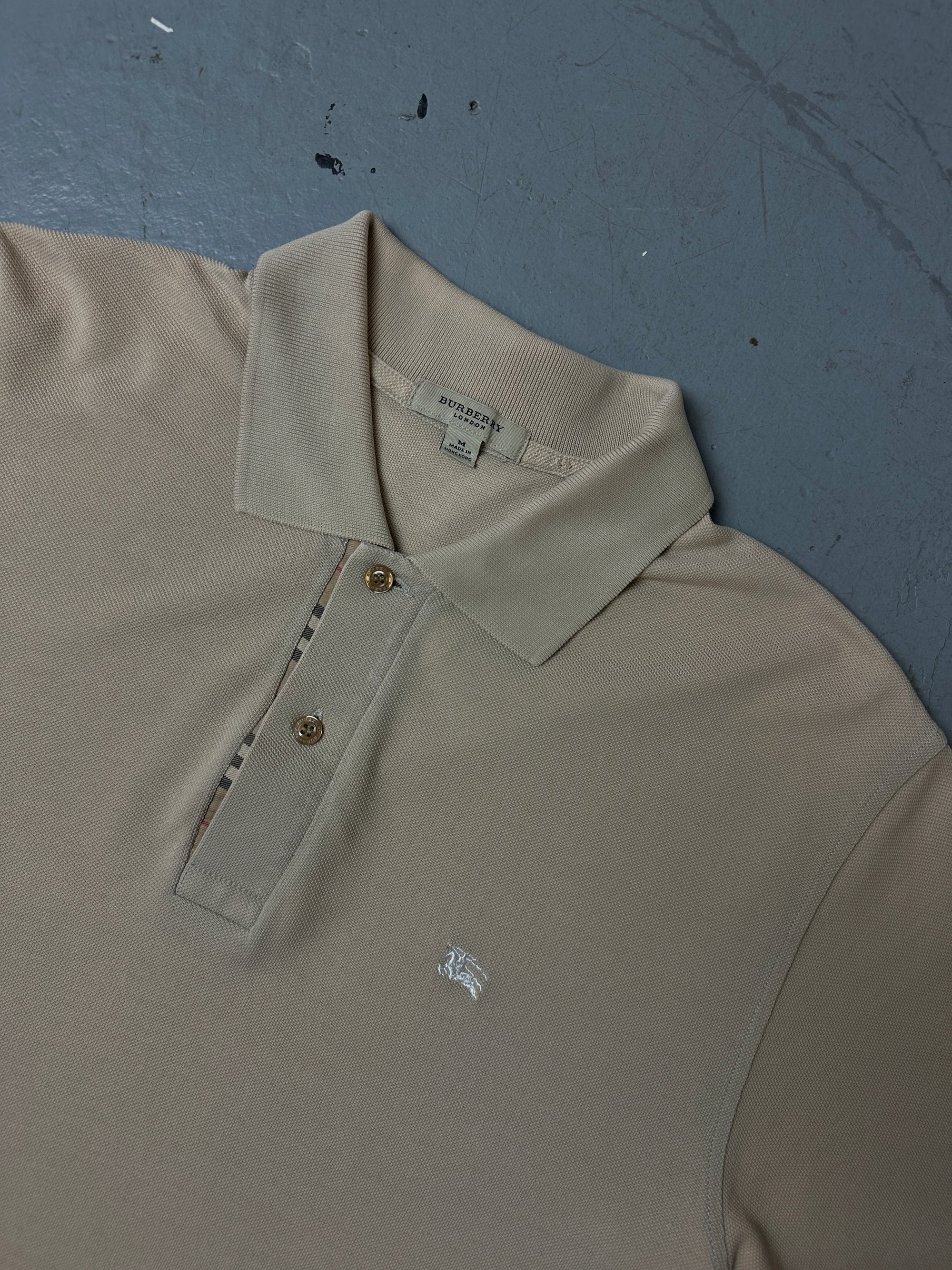 Detailliertes Produktbild von beigenen Burberry Polo auf grauem Boden 