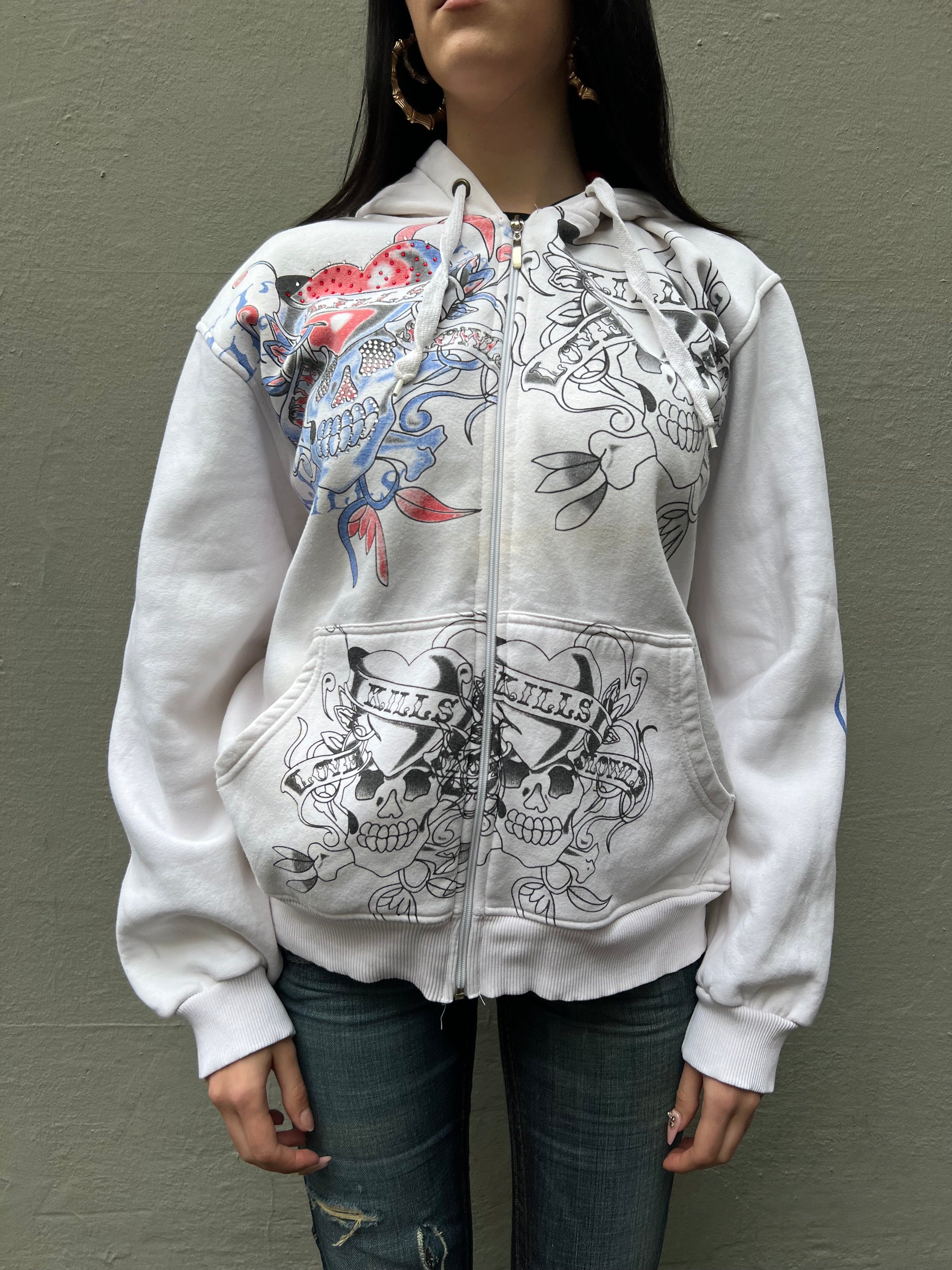 Tragebild von weißer Ed Hardy Jacke mit schwarzen und Blau-roten Aufdruck. Totenköpfe und Herzenaufdruck mit Strasssteinen auf der rechten Seite.