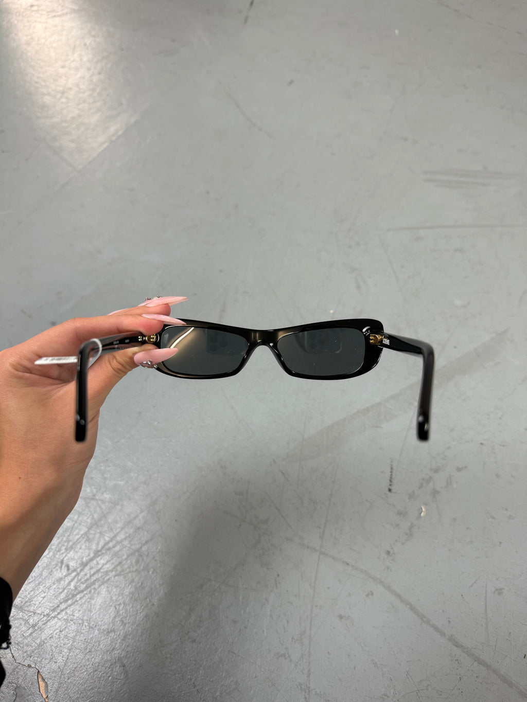 Eine schwarze schmale Sonnenbrille von Jacquemus mit goldenem Brand na,e auf den Bügeln 