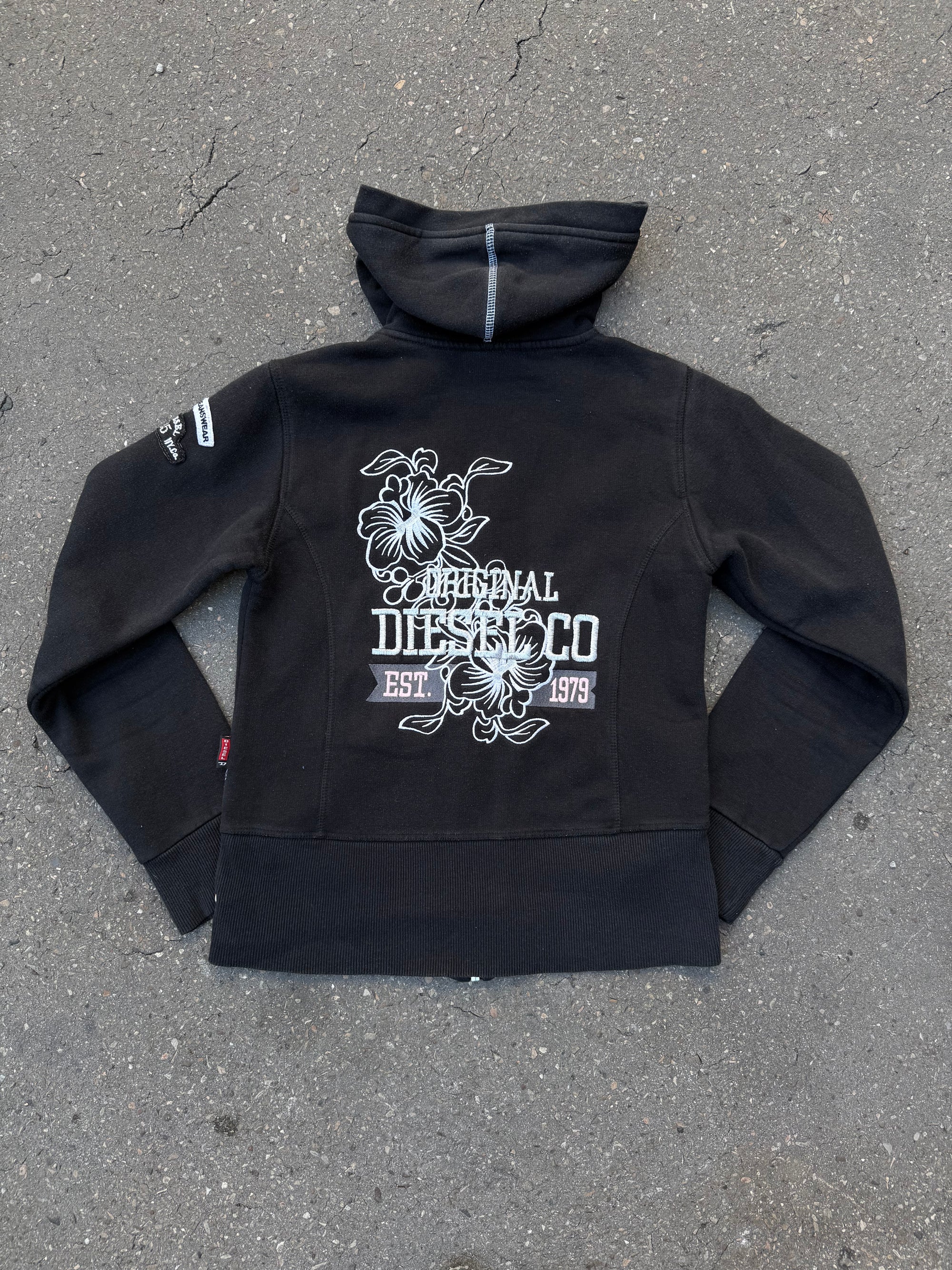 Ein schwarzer Zip Up Hoodie von Diesel mit dem Logo in weiß auf der Vorderseite und einem weißen Print auf der Rückseite