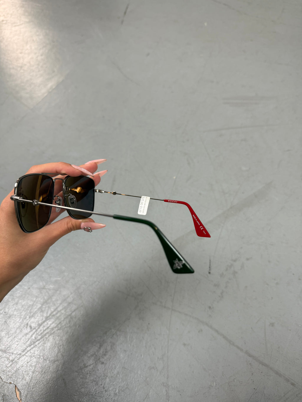 Eine eckige Sonnenbrille von gucci mit dunklen Gläsern und roten und grünen Elementen an den Bügeln 