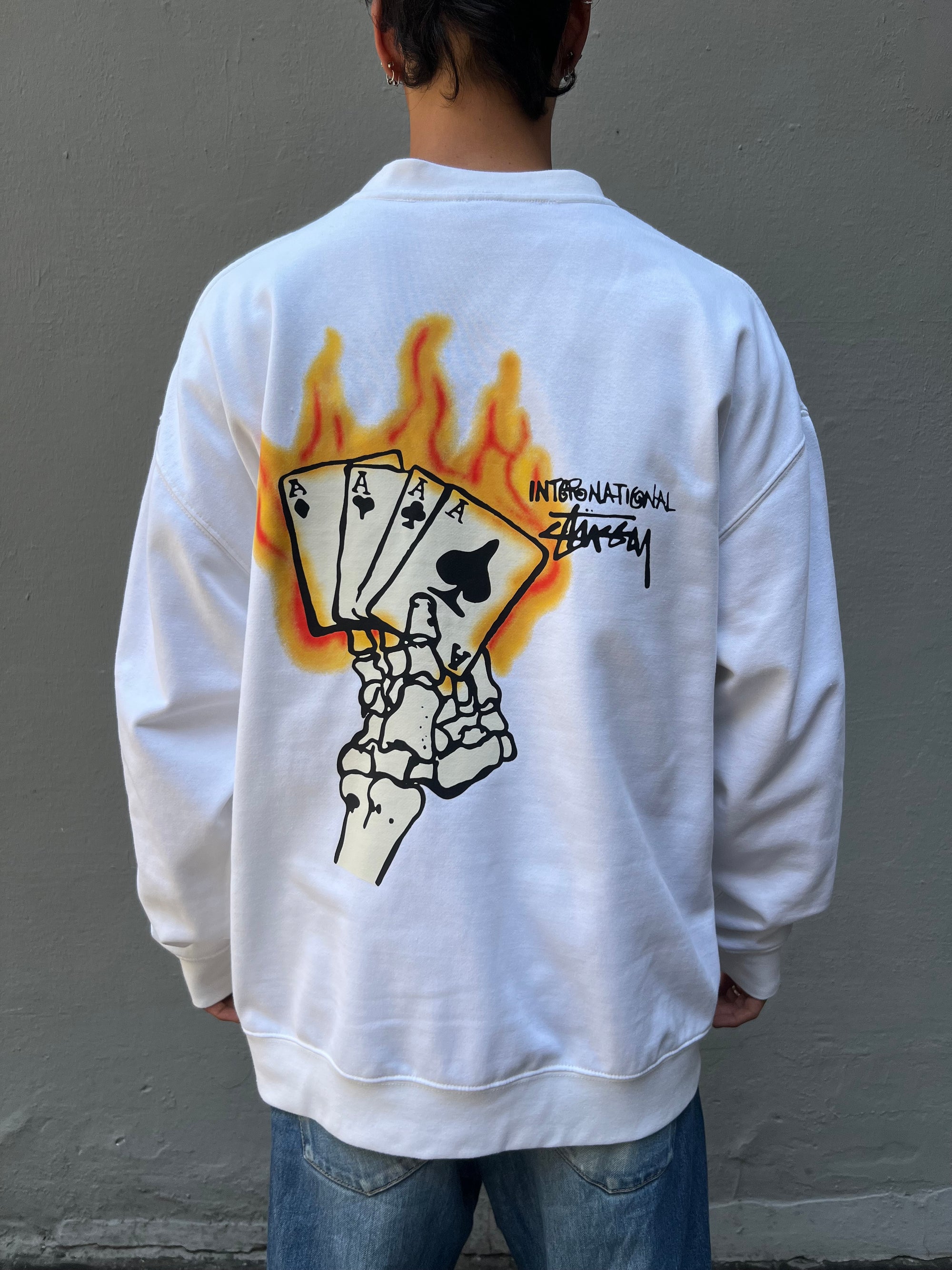 Tragebild von weißem Stüssy Longsleeve von hinten vor grauer Wand
