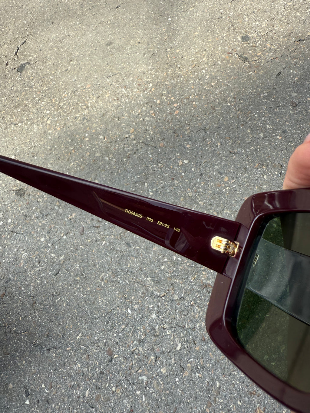 Eine burgunderrote Sonnenbrille von Gucci mit dem Logo in Gold an der Seite und großen quadratischen Gläsern