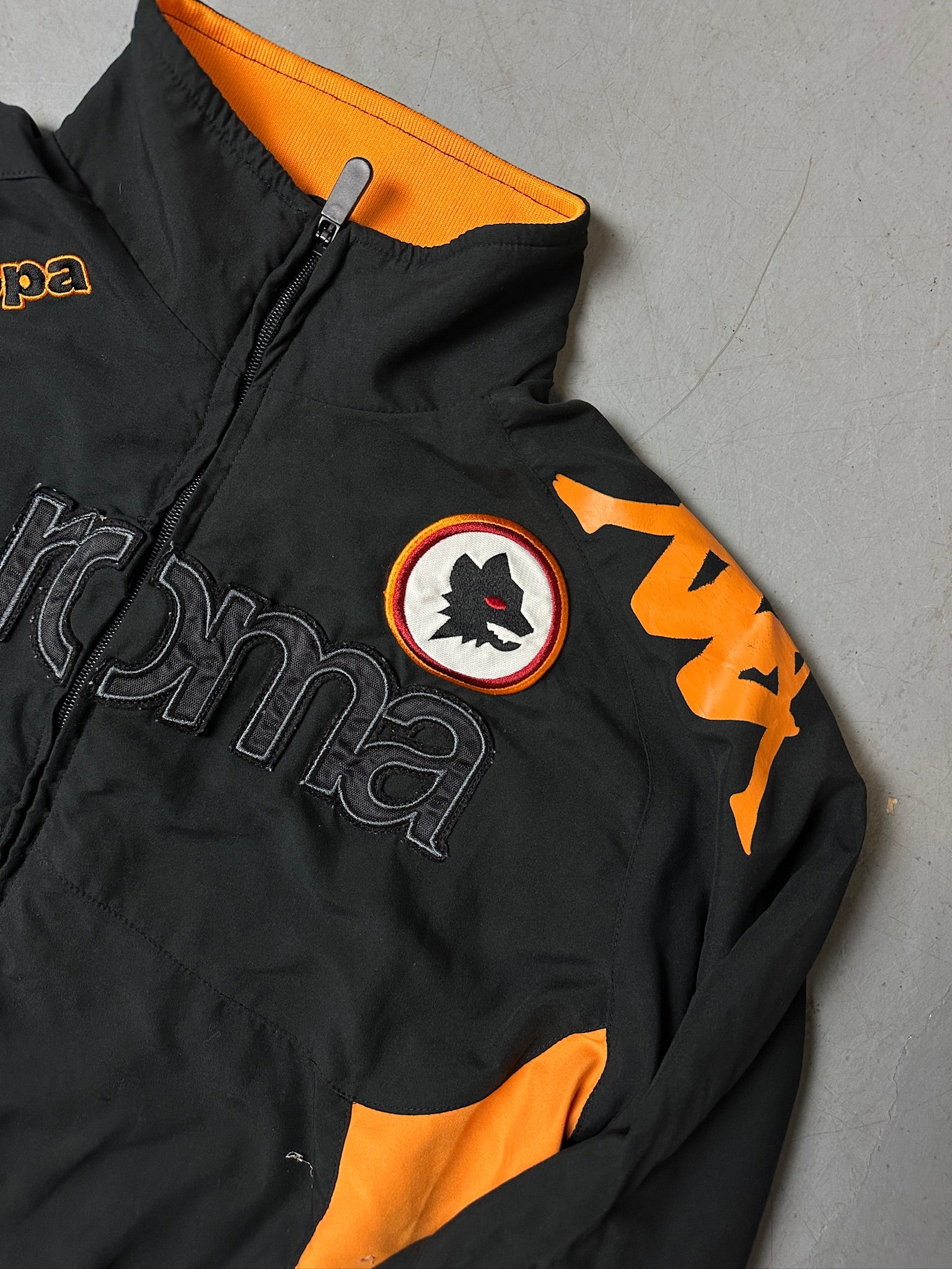 Eine schwarz orange Track Jacke von kappa von dem Fußballverein as roma 