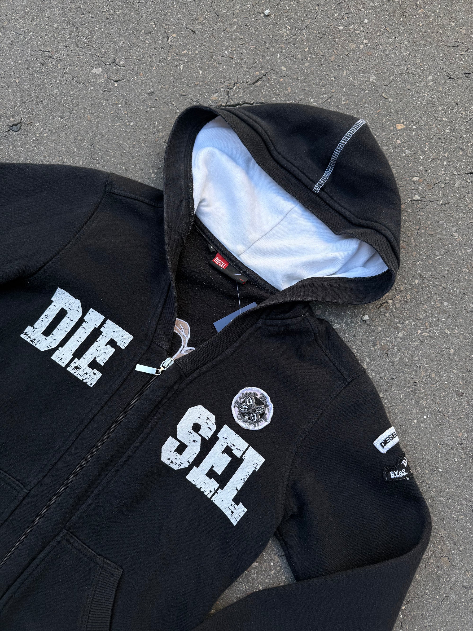 Ein schwarzer Zip Up Hoodie von Diesel mit dem Logo in weiß auf der Vorderseite und einem weißen Print auf der Rückseite