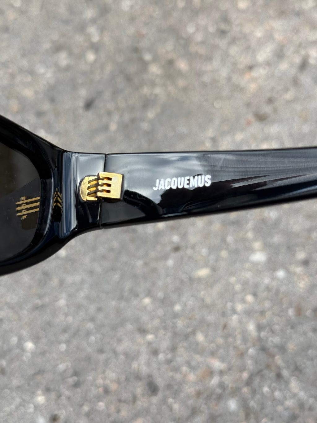 Eine schwarze Sonnenbrille von Jacquemus mit goldenem Schriftzug auf der Seite