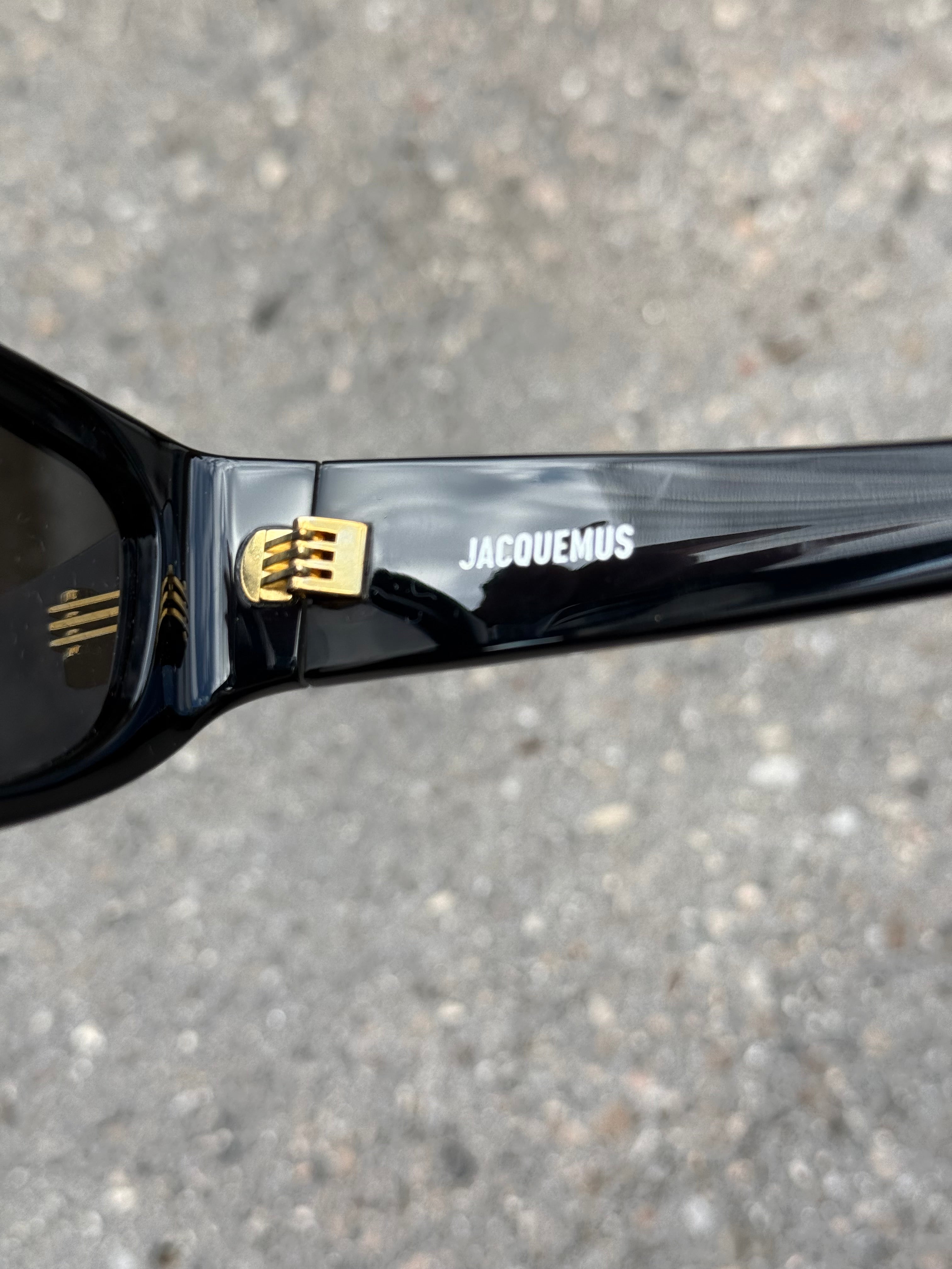 Eine schwarze Sonnenbrille von Jacquemus mit goldenem Schriftzug auf der Seite